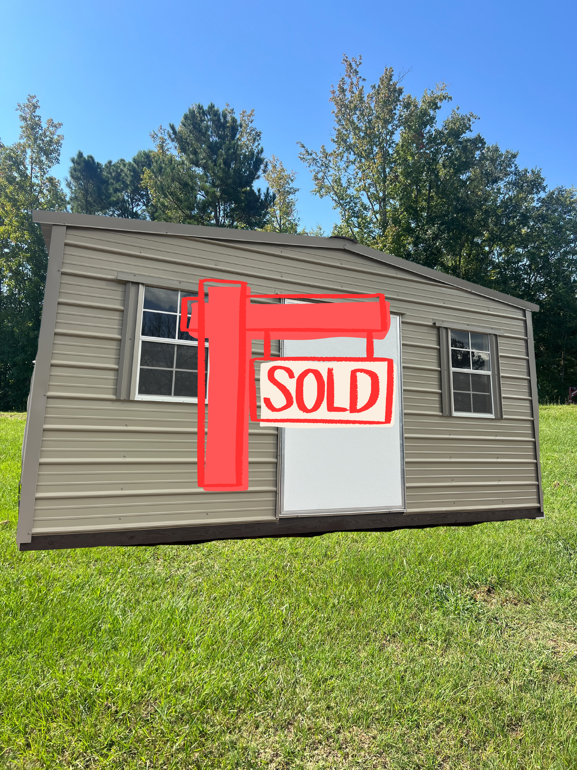 Tan shed with white door and windows on a grassy lawn with trees in the background.