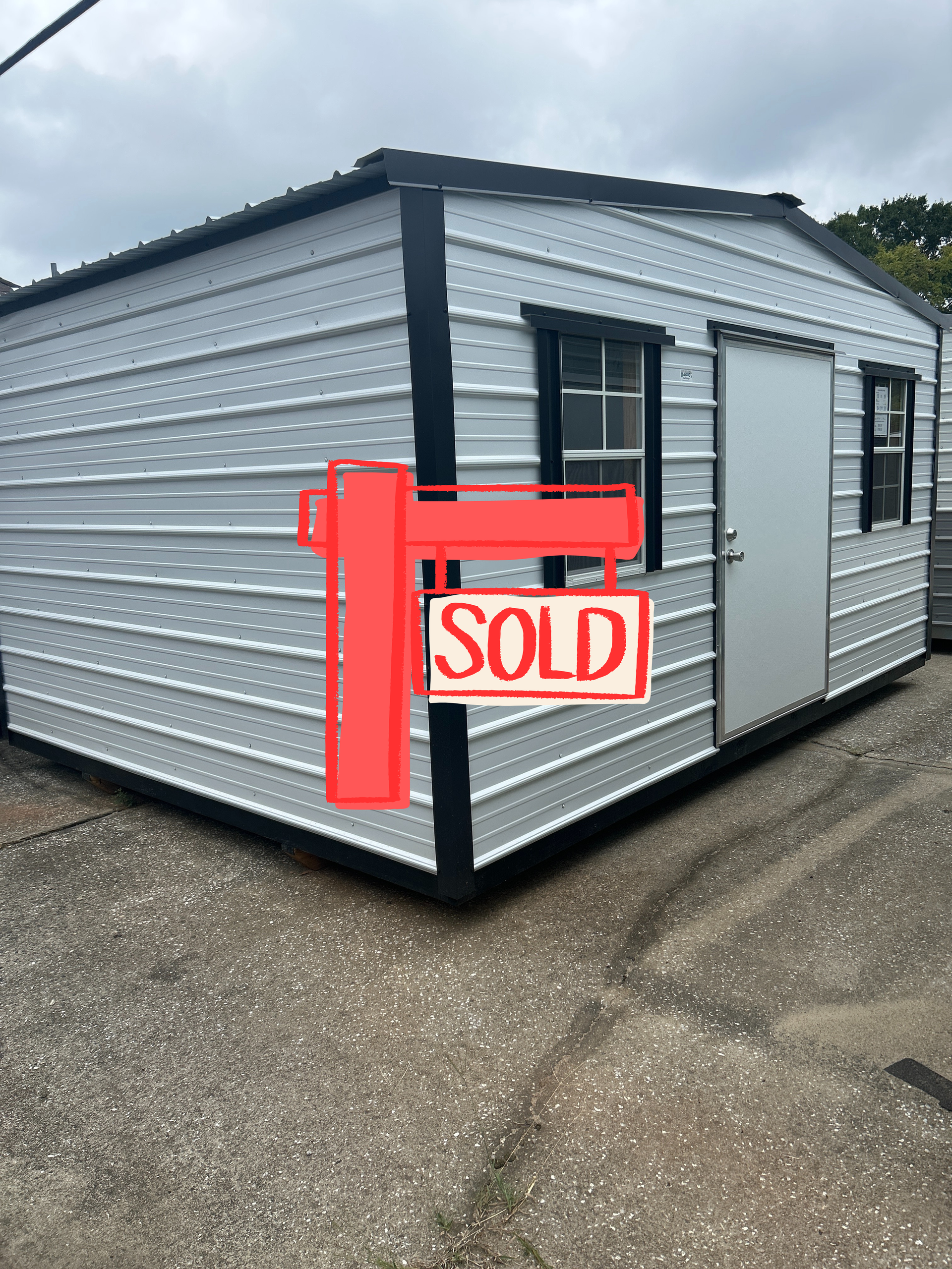 White metal shed with black trim, door, and two windows, sitting on gravel.