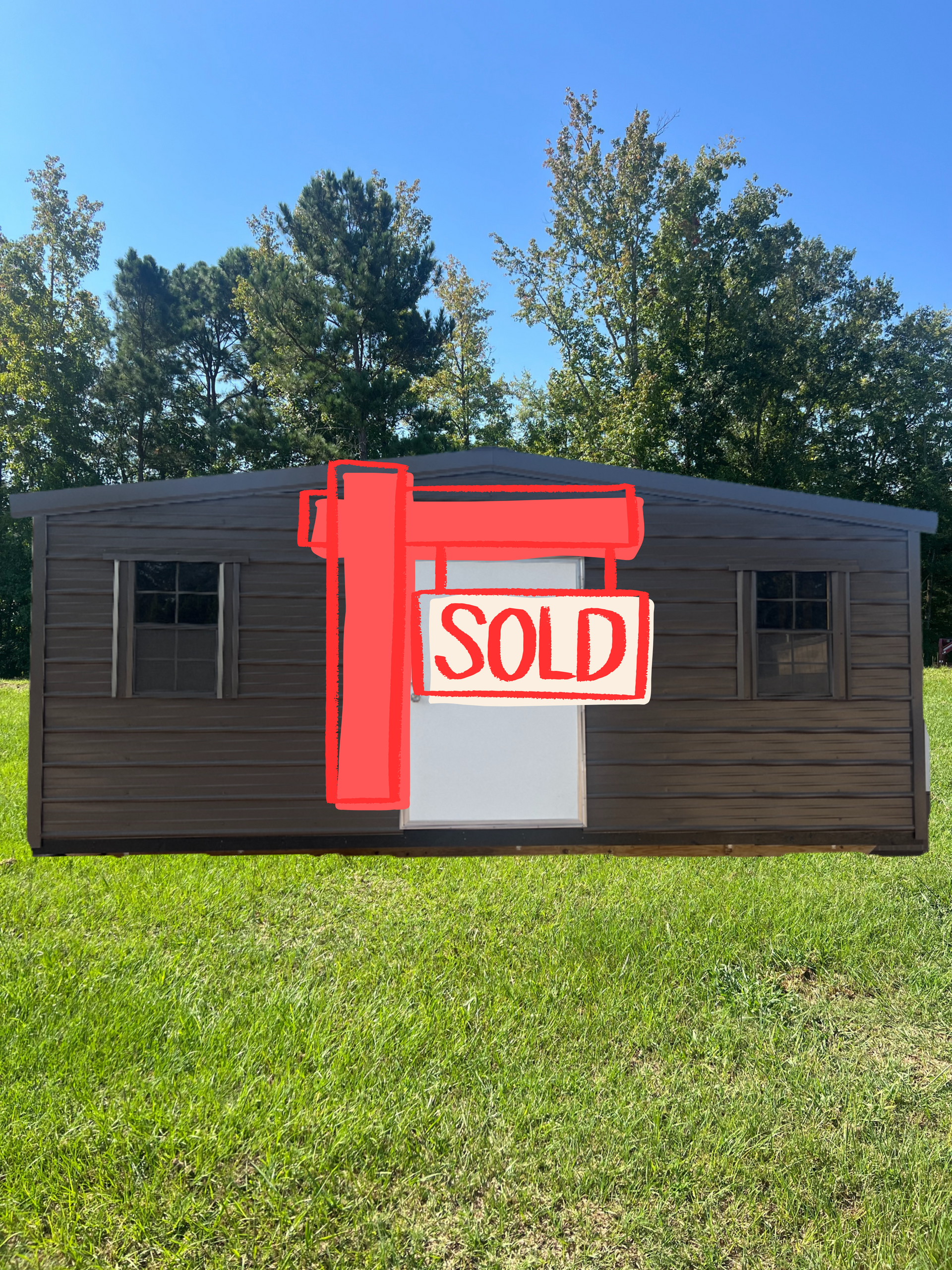 Brown shed with white door and two small windows on green grass, trees in background.