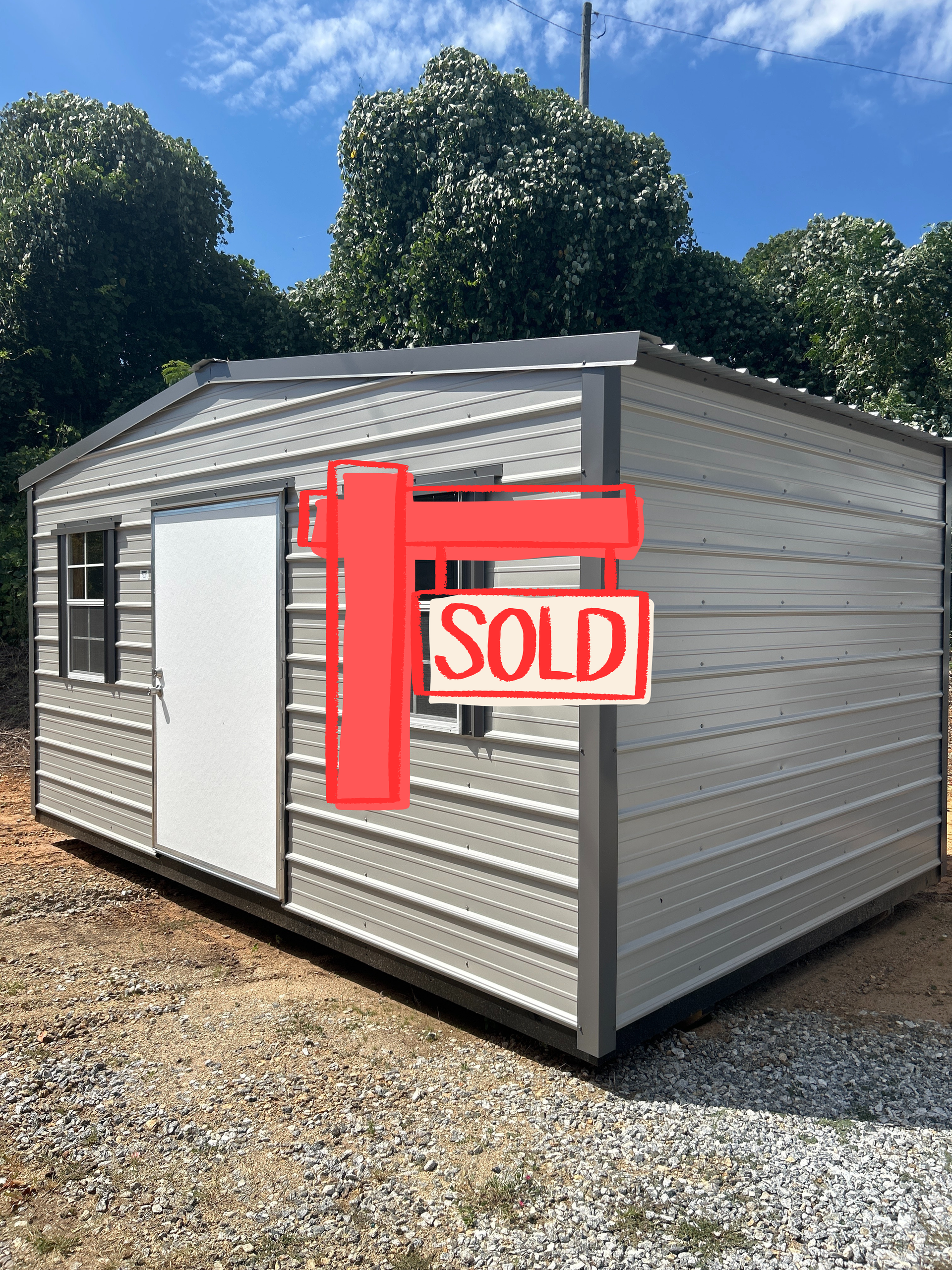 Gray metal shed with white door and windows, outdoors on a gravel surface.