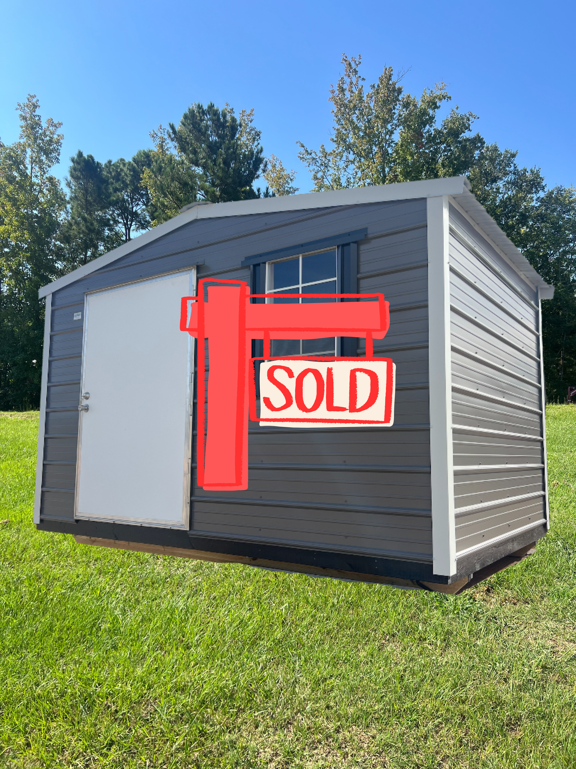 Gray and white storage shed on green grass under a blue sky. A white door and a window are visible.