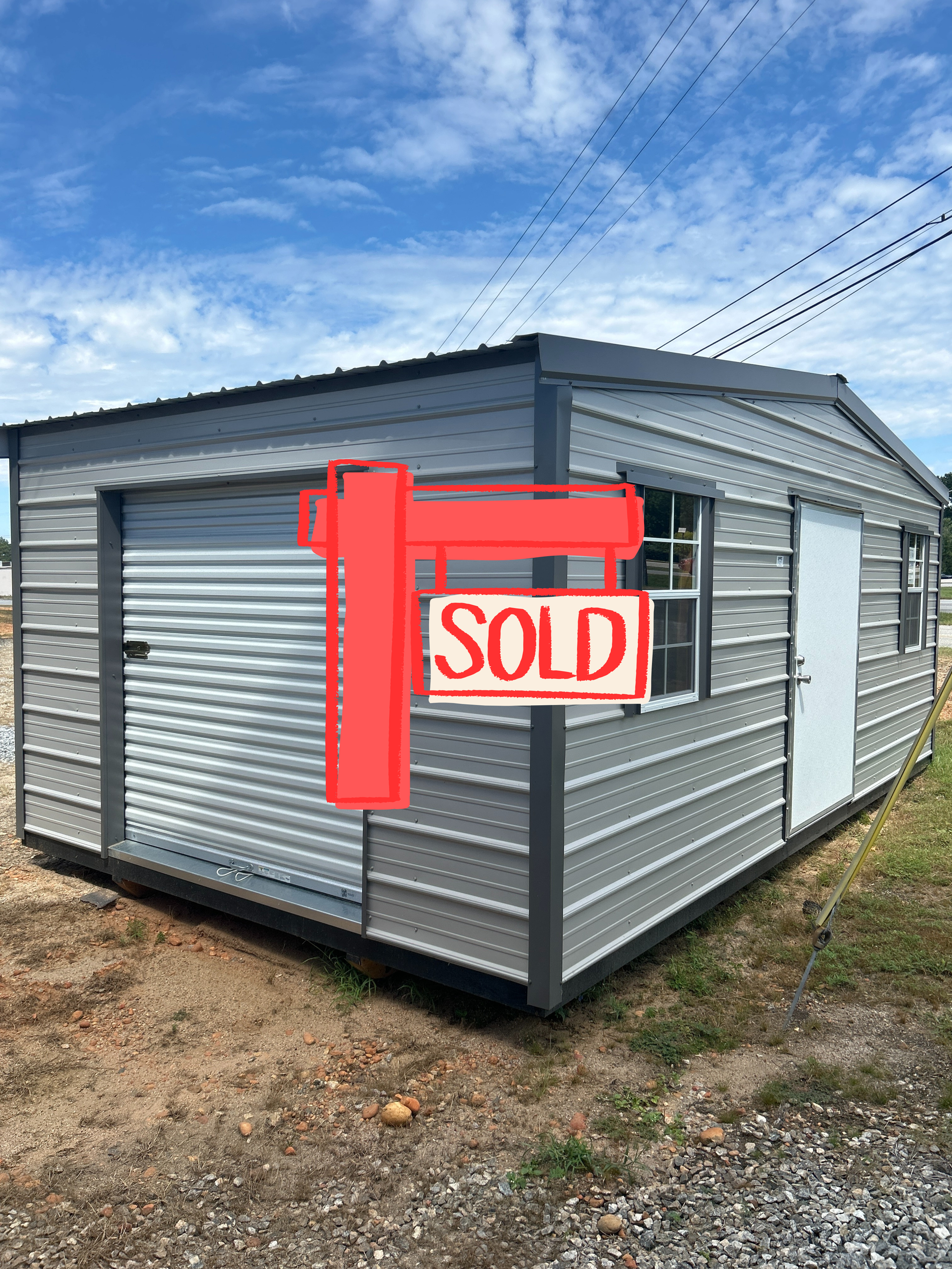 Gray metal shed with a roll-up door, window, and a regular door under a blue sky.