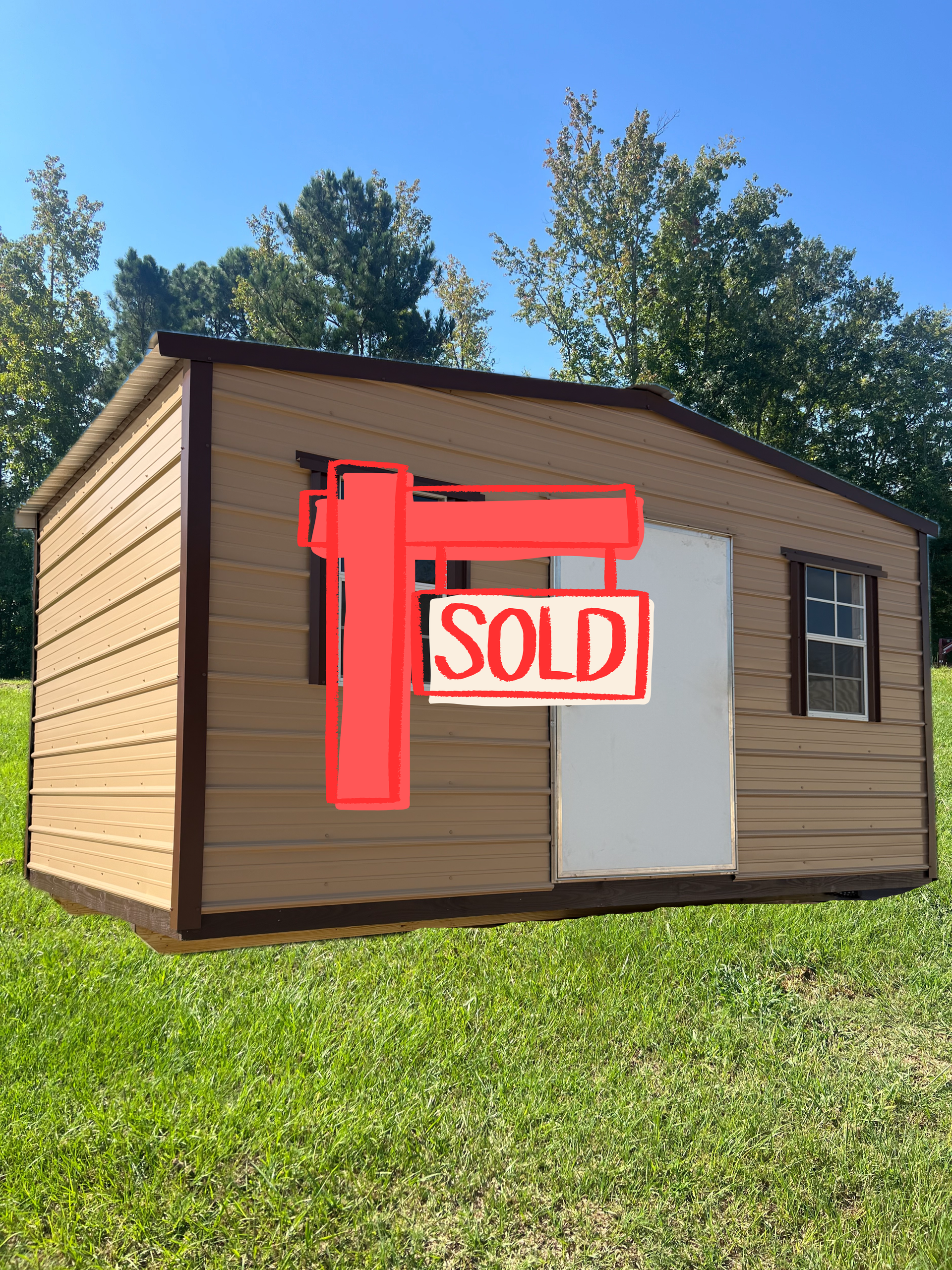 Tan shed with brown trim, a single white door, and two windows sitting on a grassy lawn under a clear blue sky.