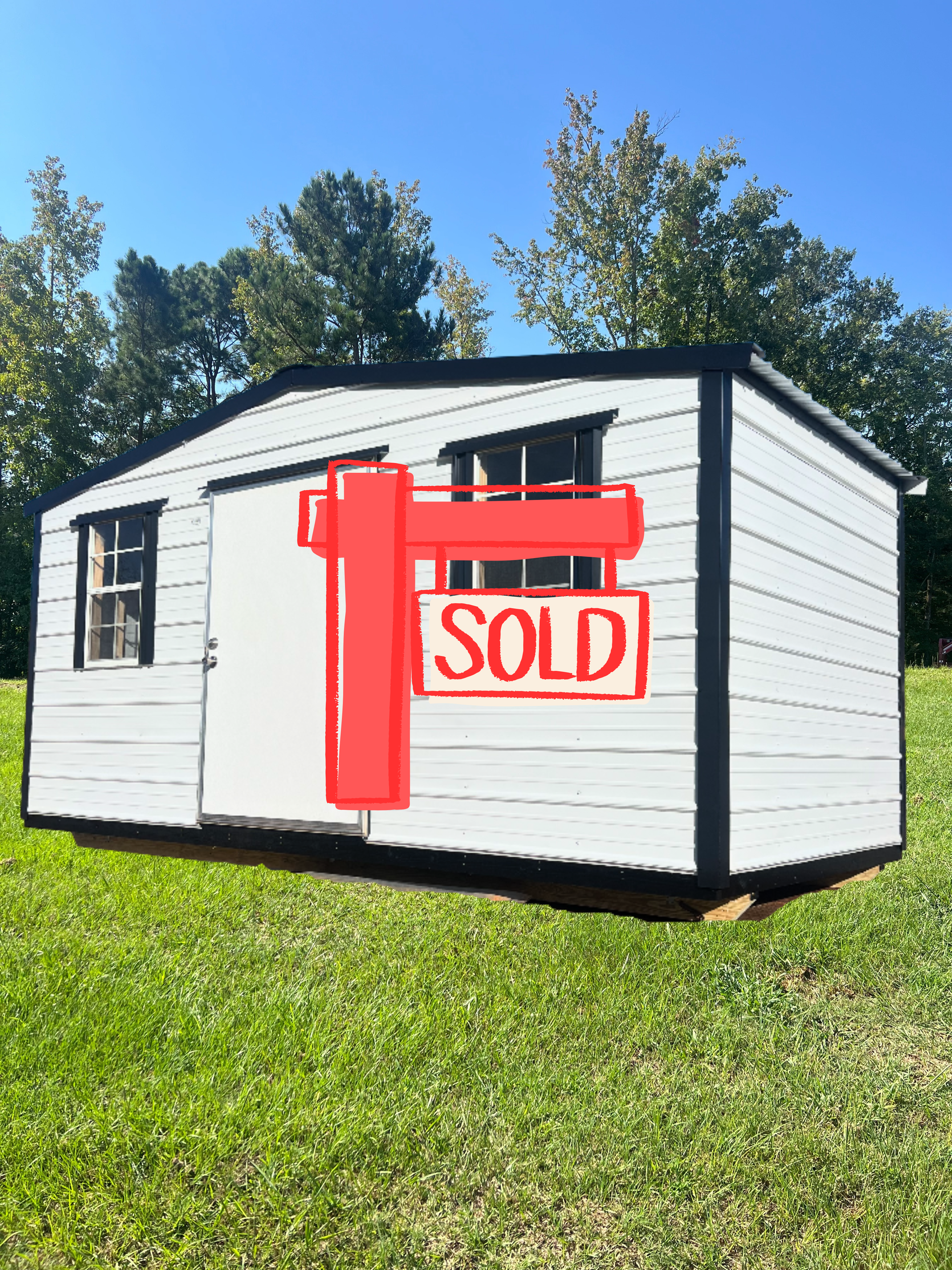 White shed with black trim and two windows on green grass.