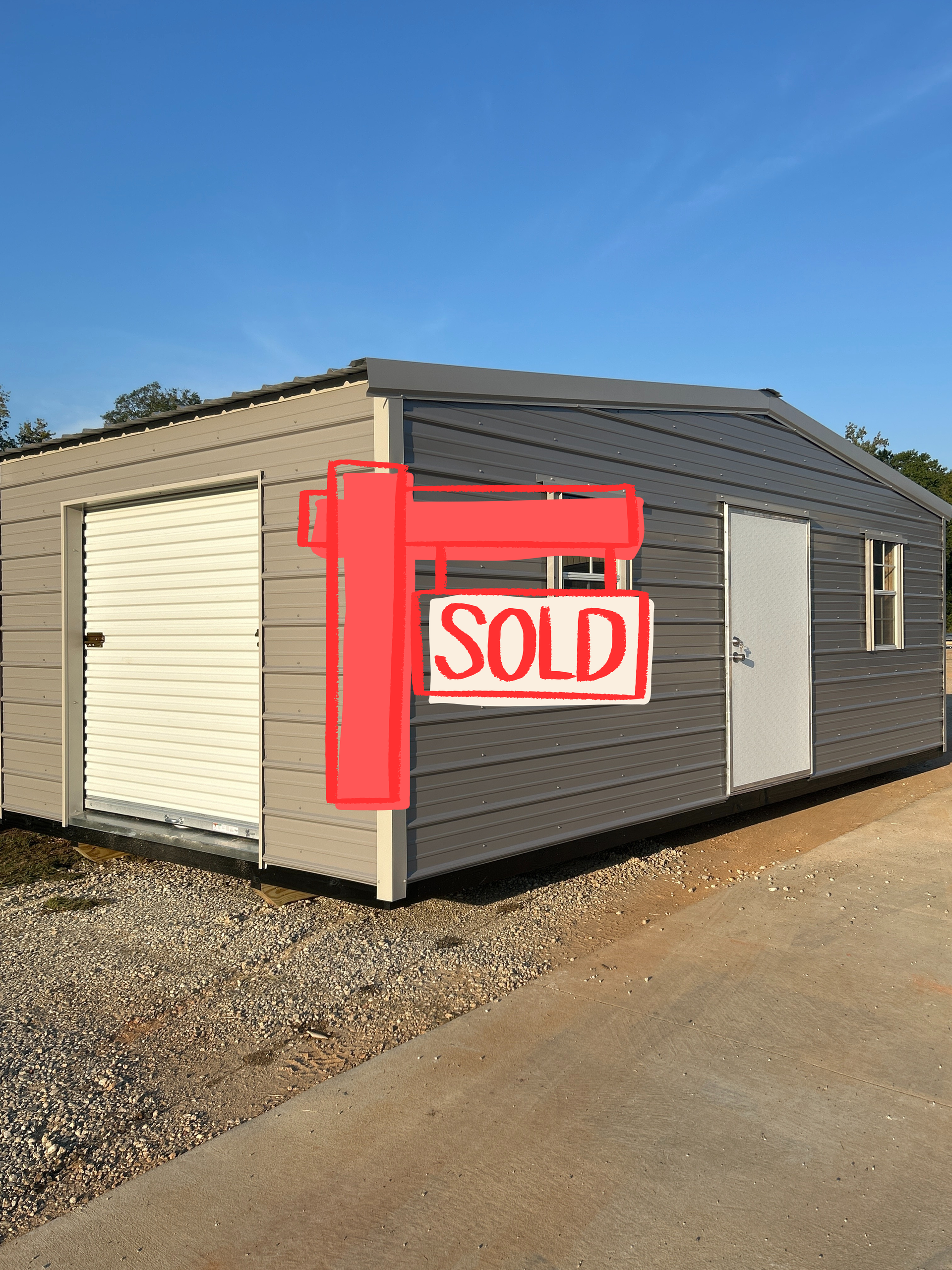 Gray metal shed with white doors and windows, set on gravel.