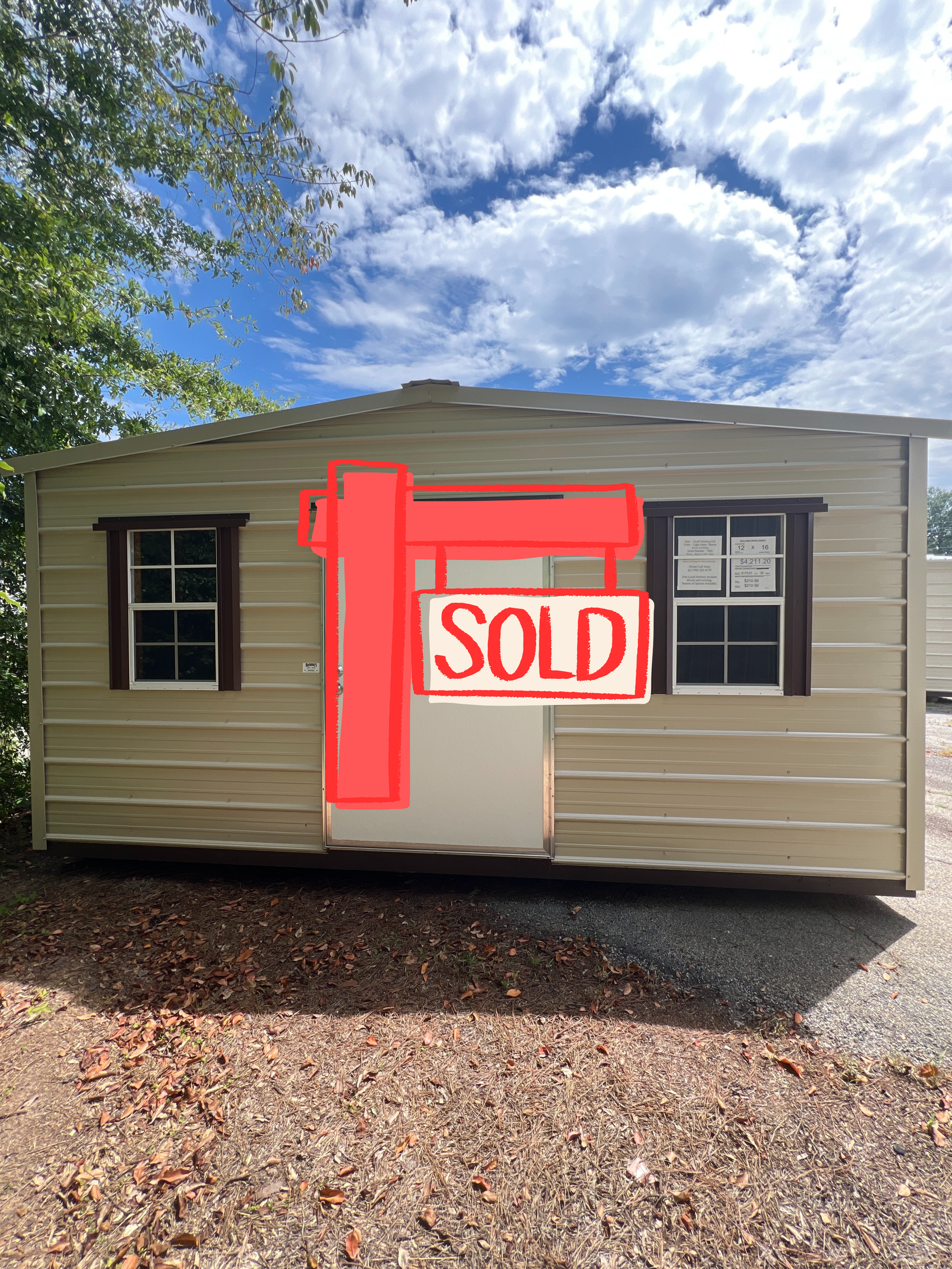 Tan shed with white door and windows, under a blue sky with clouds.