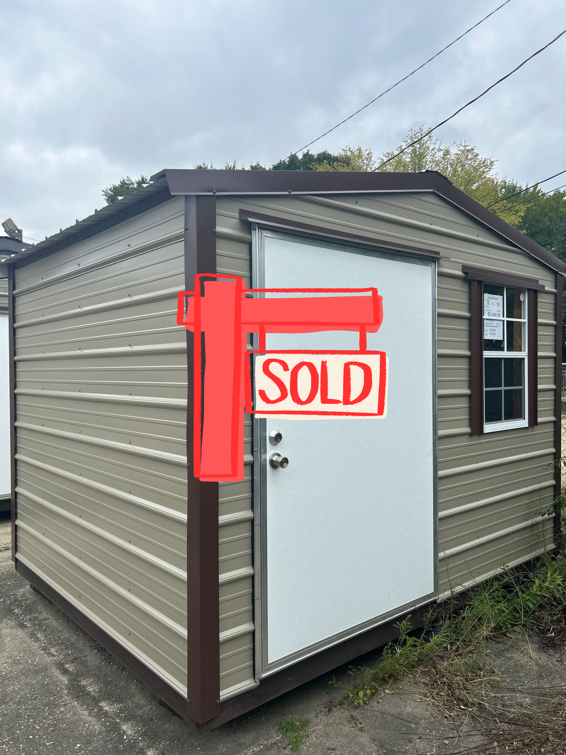 Tan and brown metal storage shed with white door and window. Set outdoors on a cloudy day.