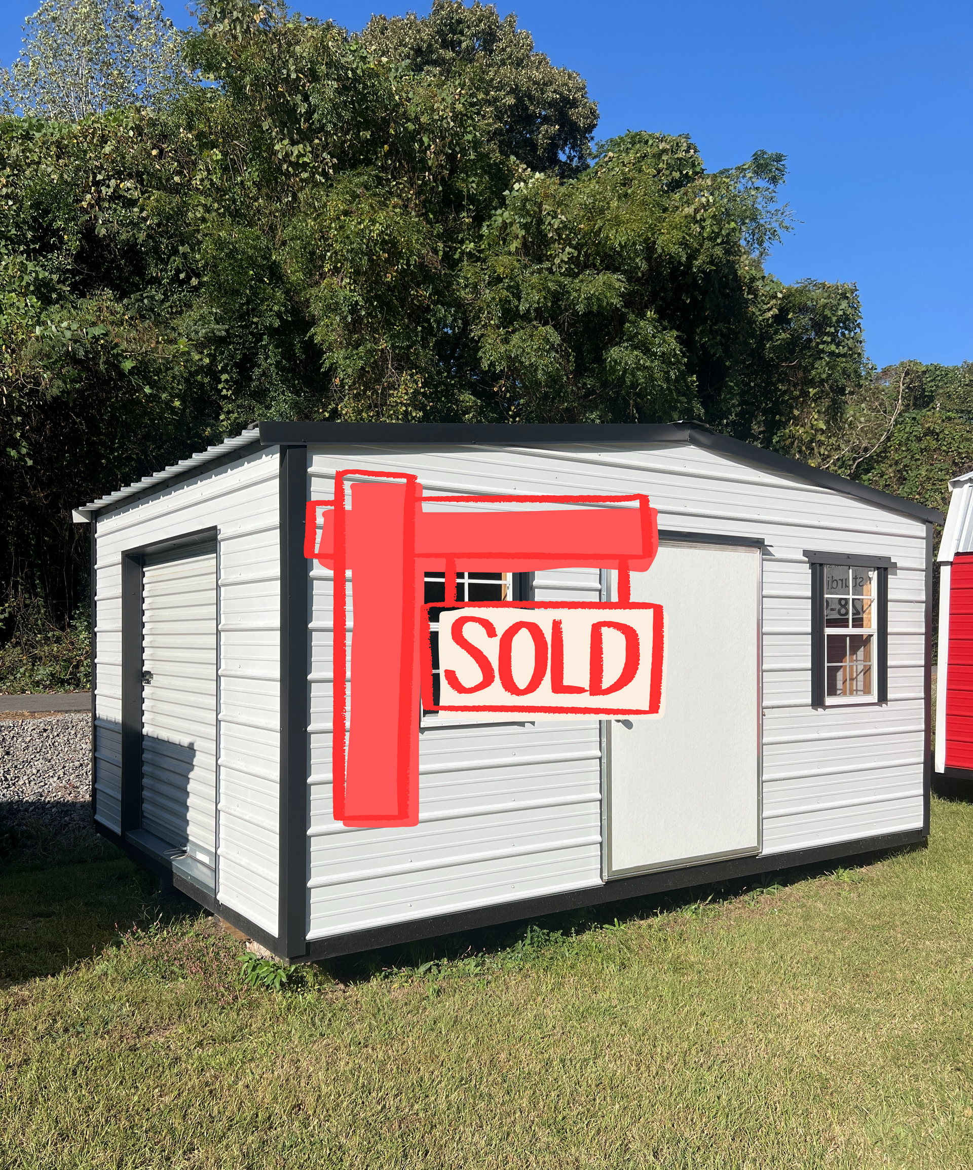 Gray shed with dark brown trim, windows, and door on a grassy lawn under a blue sky.