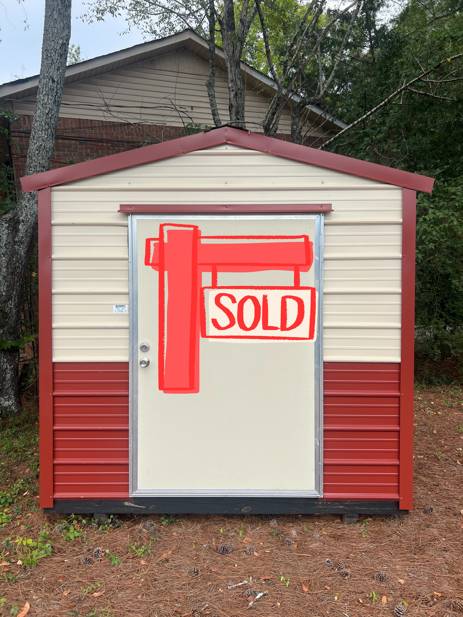 Red and beige metal storage shed with a closed door, outdoors.