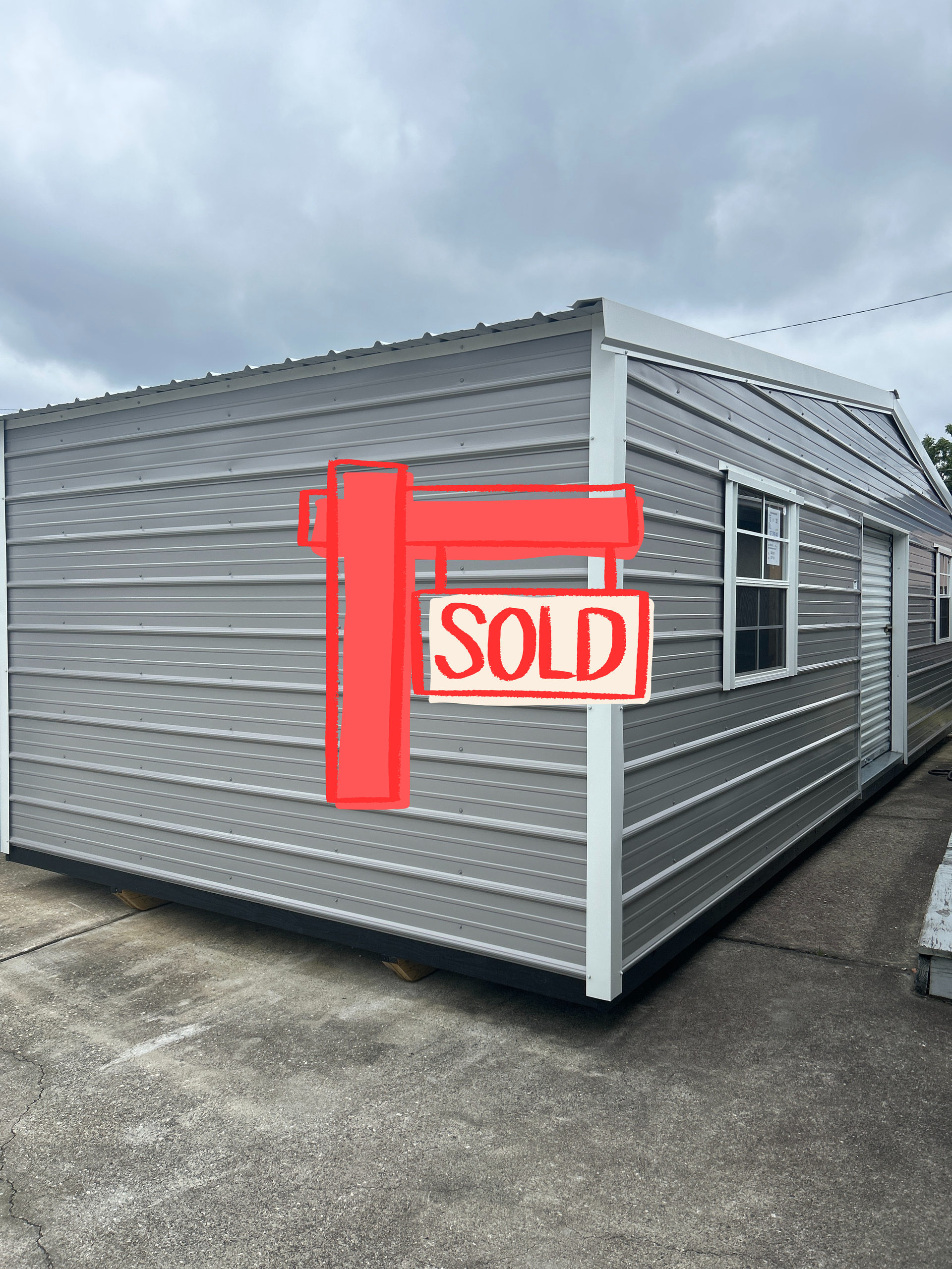 Gray metal building with white trim, windows, and door against a cloudy sky.