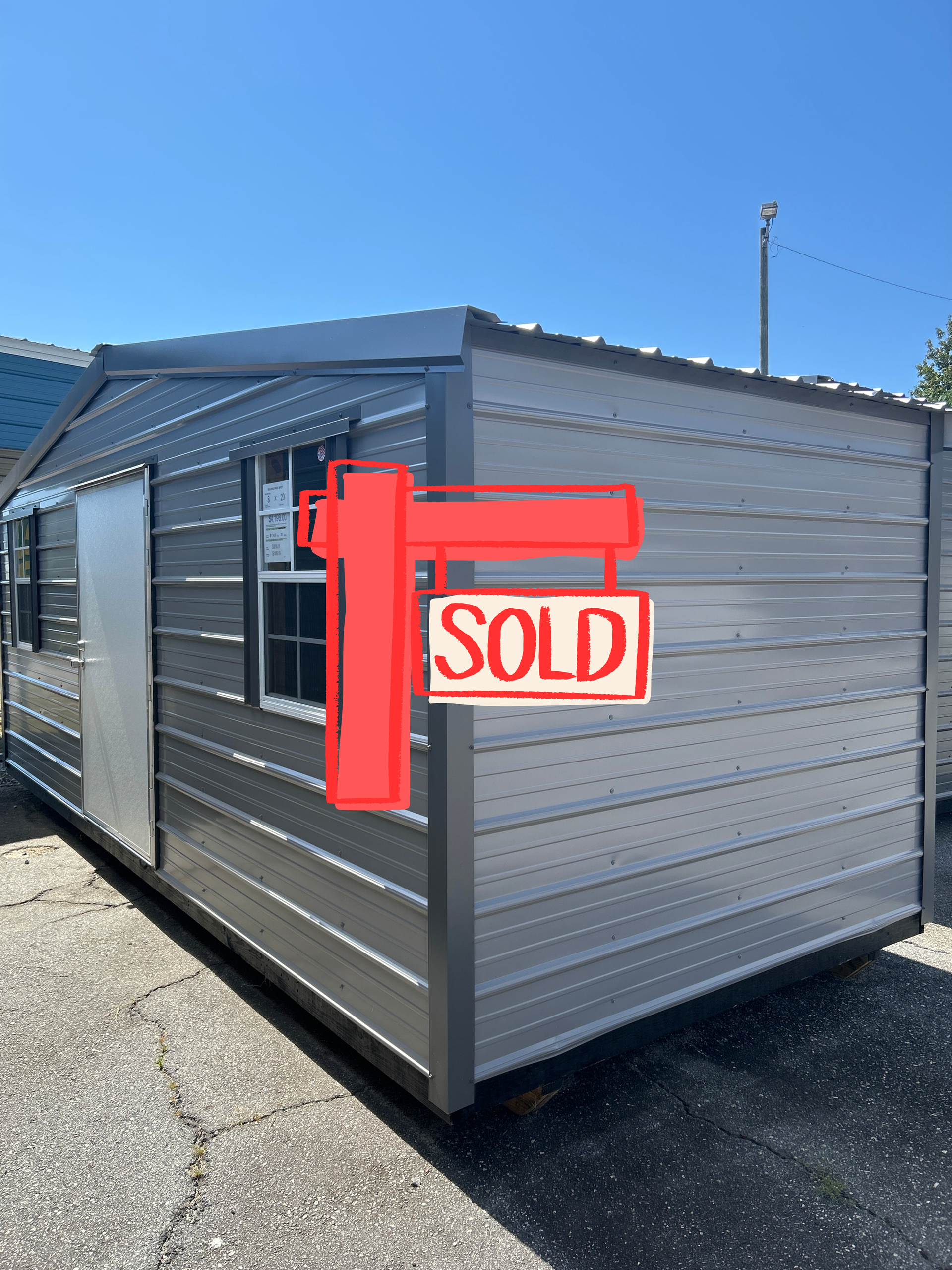 Gray metal shed with door and window on a sunny day.