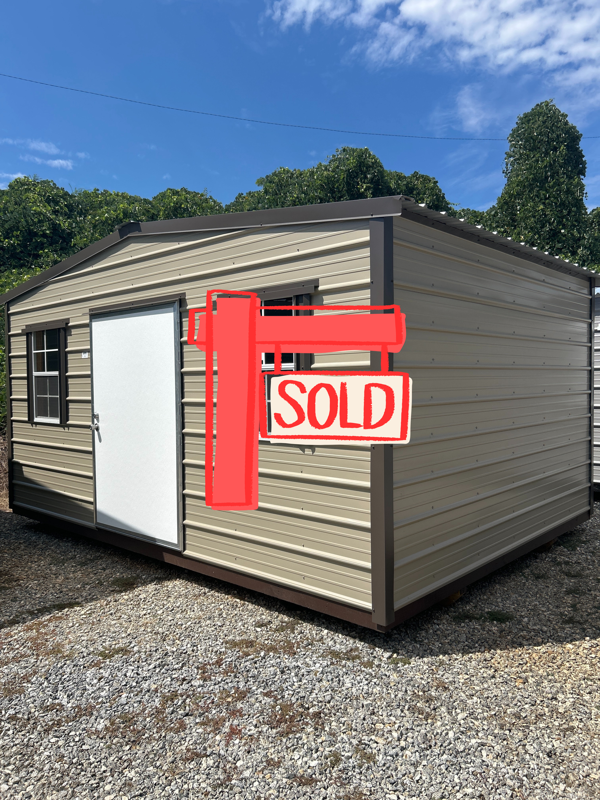 Tan metal shed with brown trim, white door, and two windows, set on gravel.