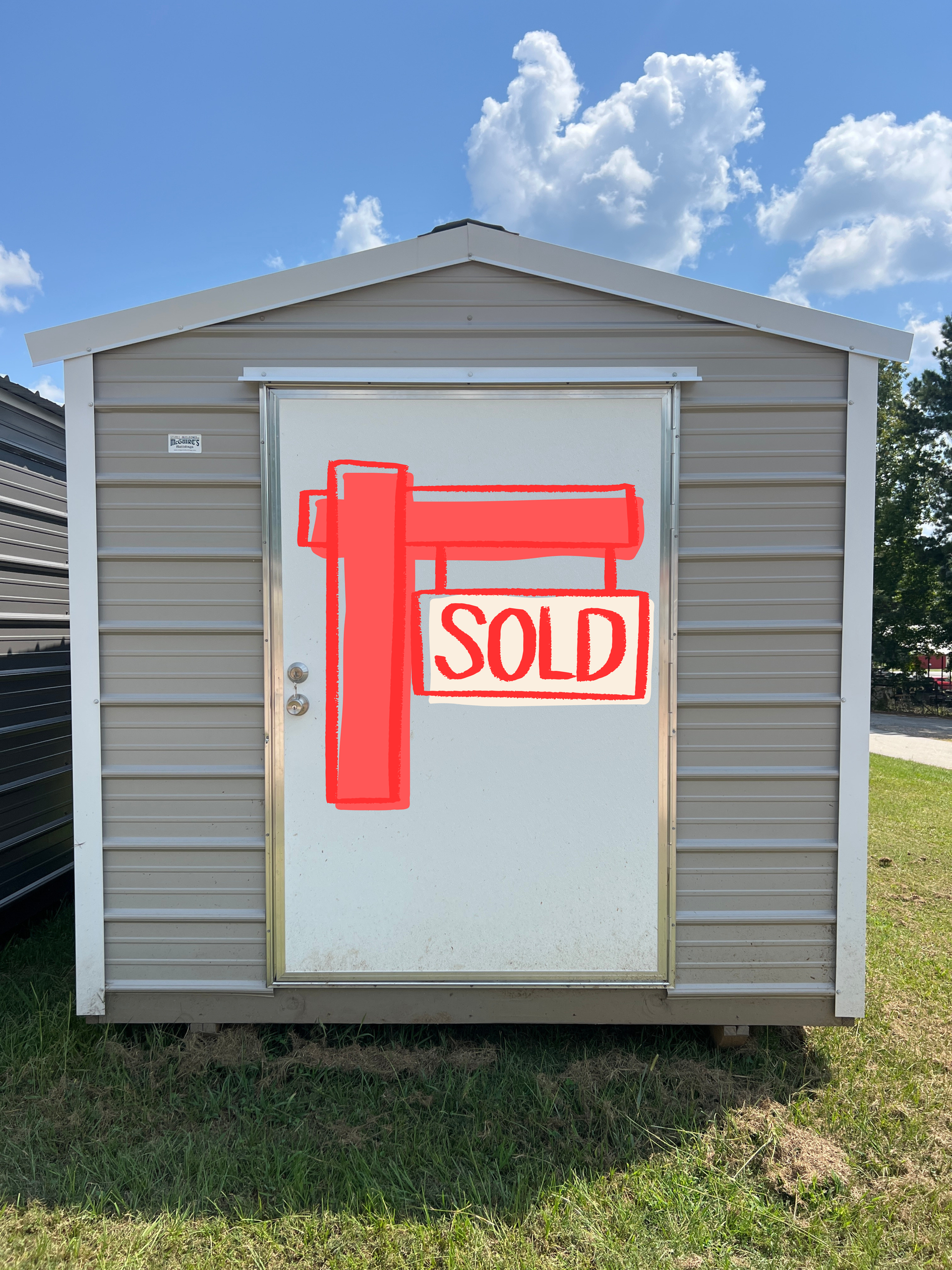 Gray shed with white door, set on green grass, against a blue sky with clouds.