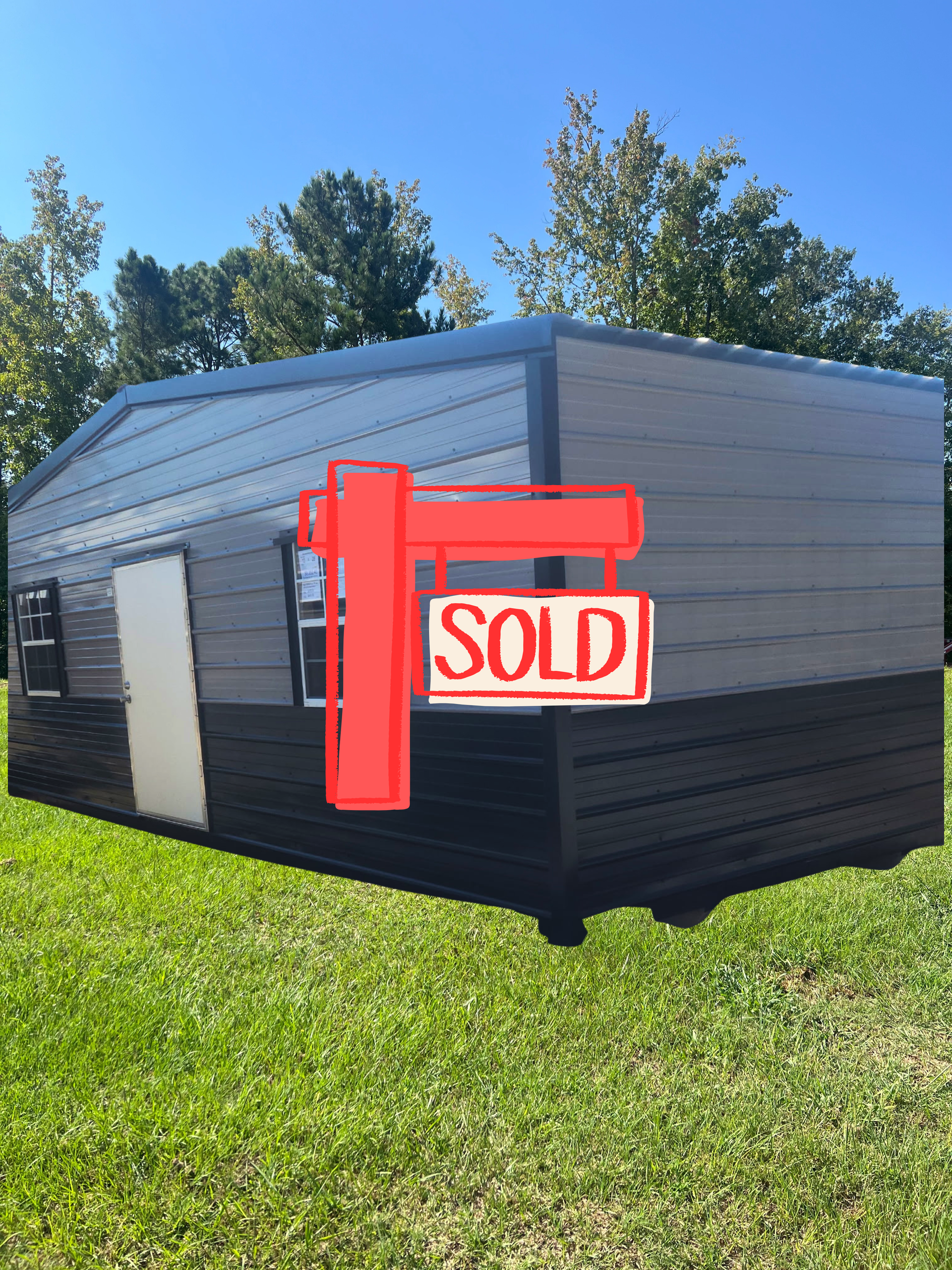 Small black and gray portable building on grass with a red “SOLD” sign on the front