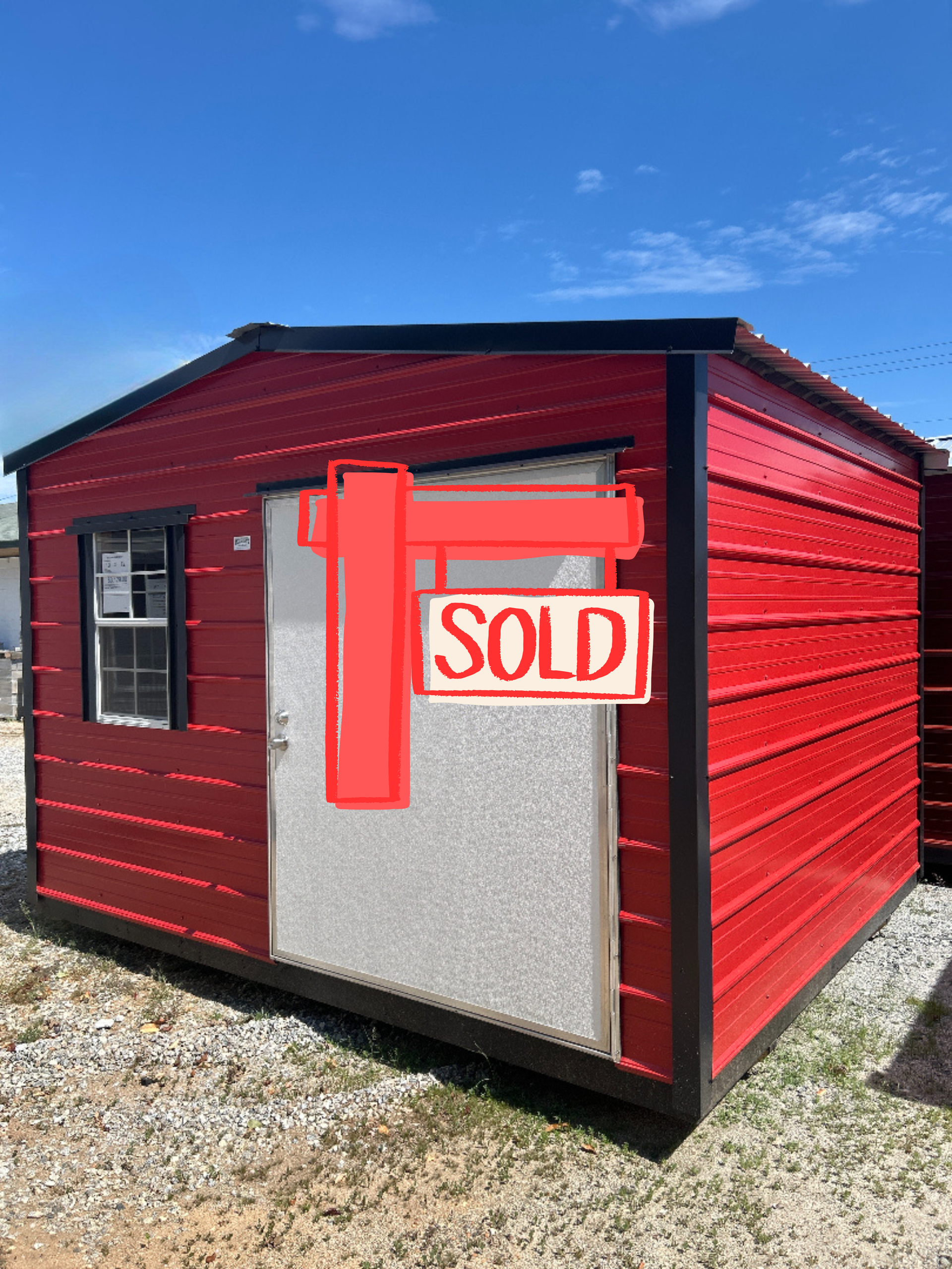 Red and black shed with a white door and small window against a blue sky.