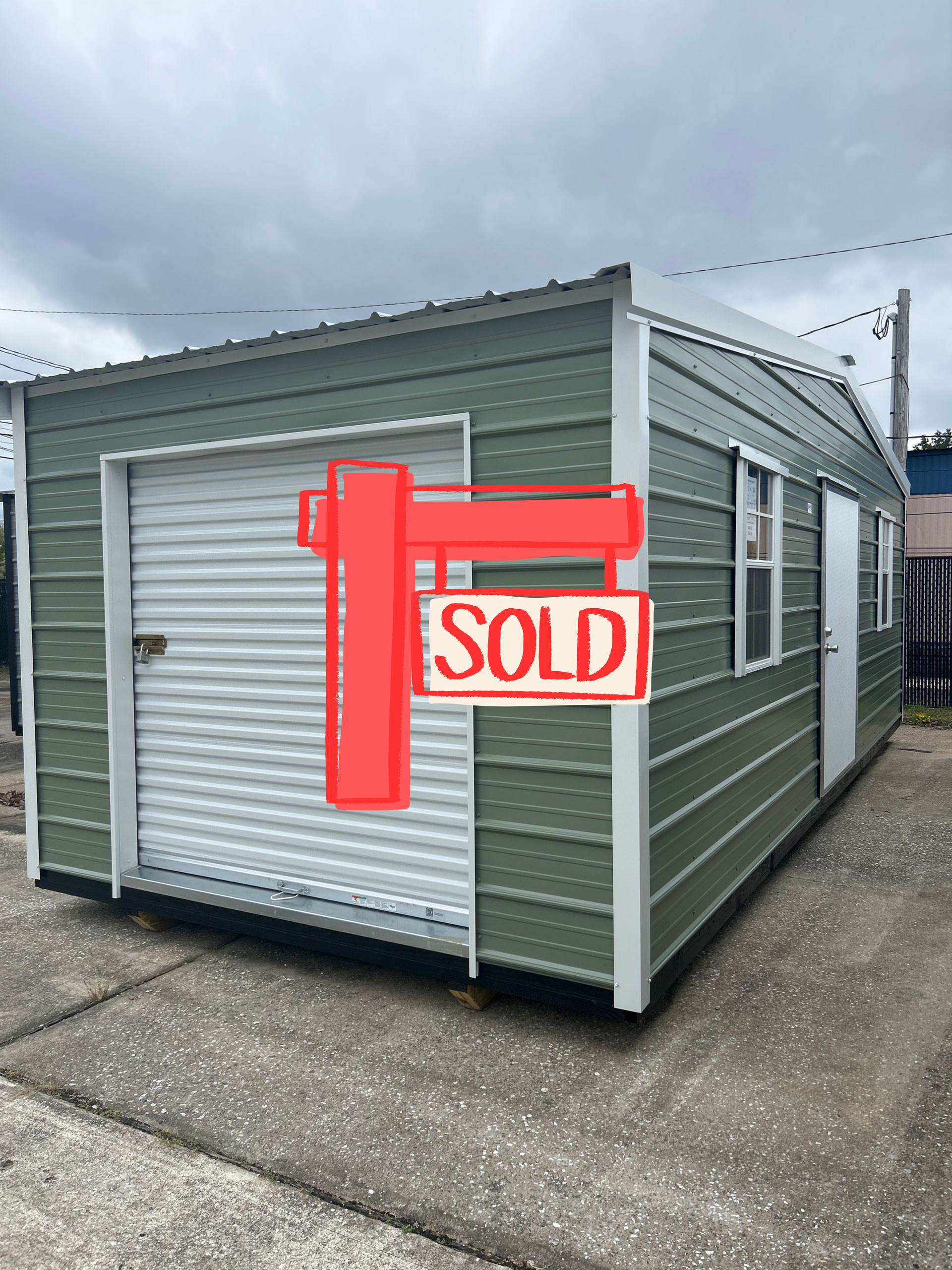 Green metal storage shed with a roll-up door and small windows, on a concrete surface.