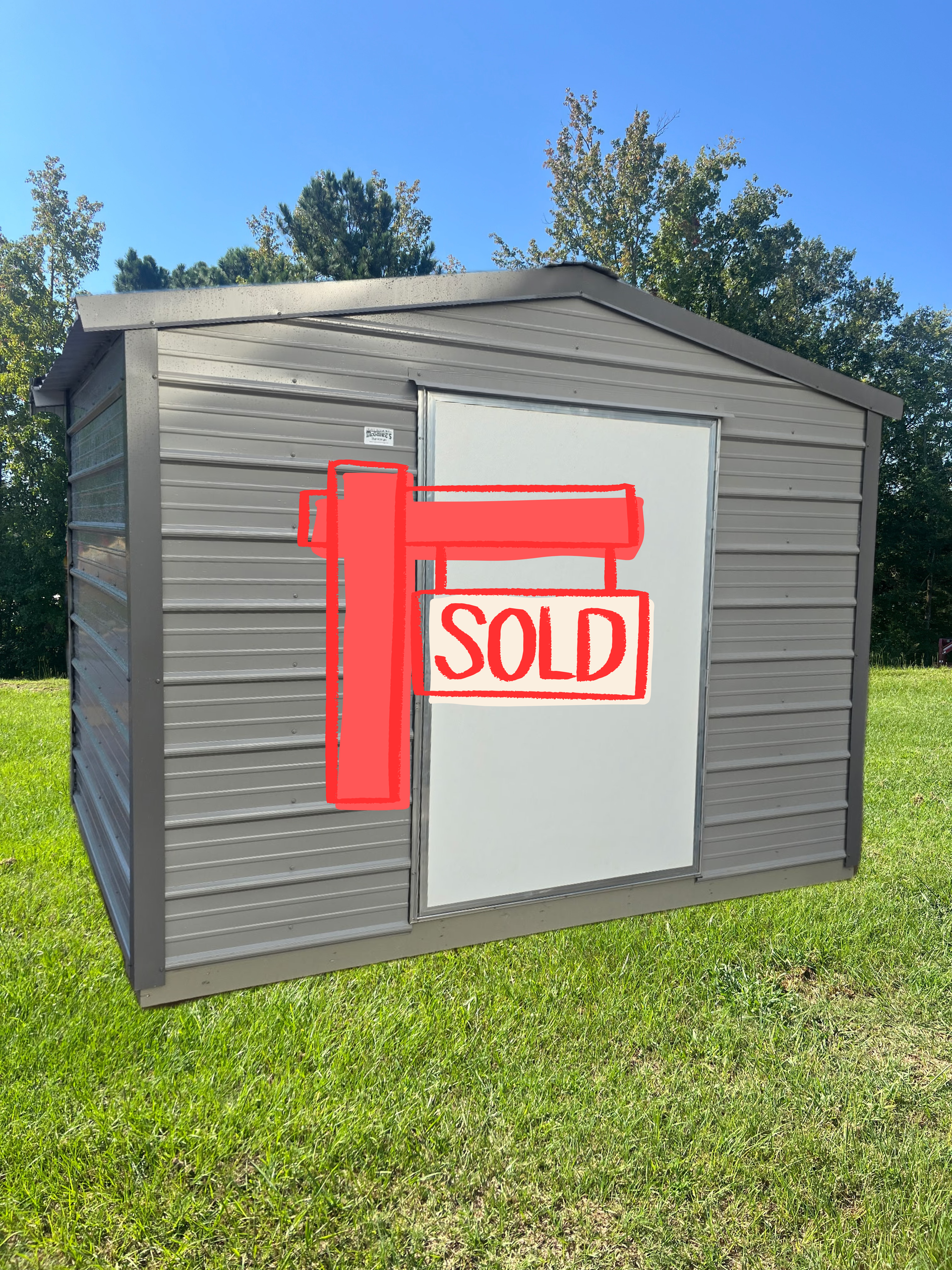 Gray shed with a white door and a red SOLD sign in a sunny yard