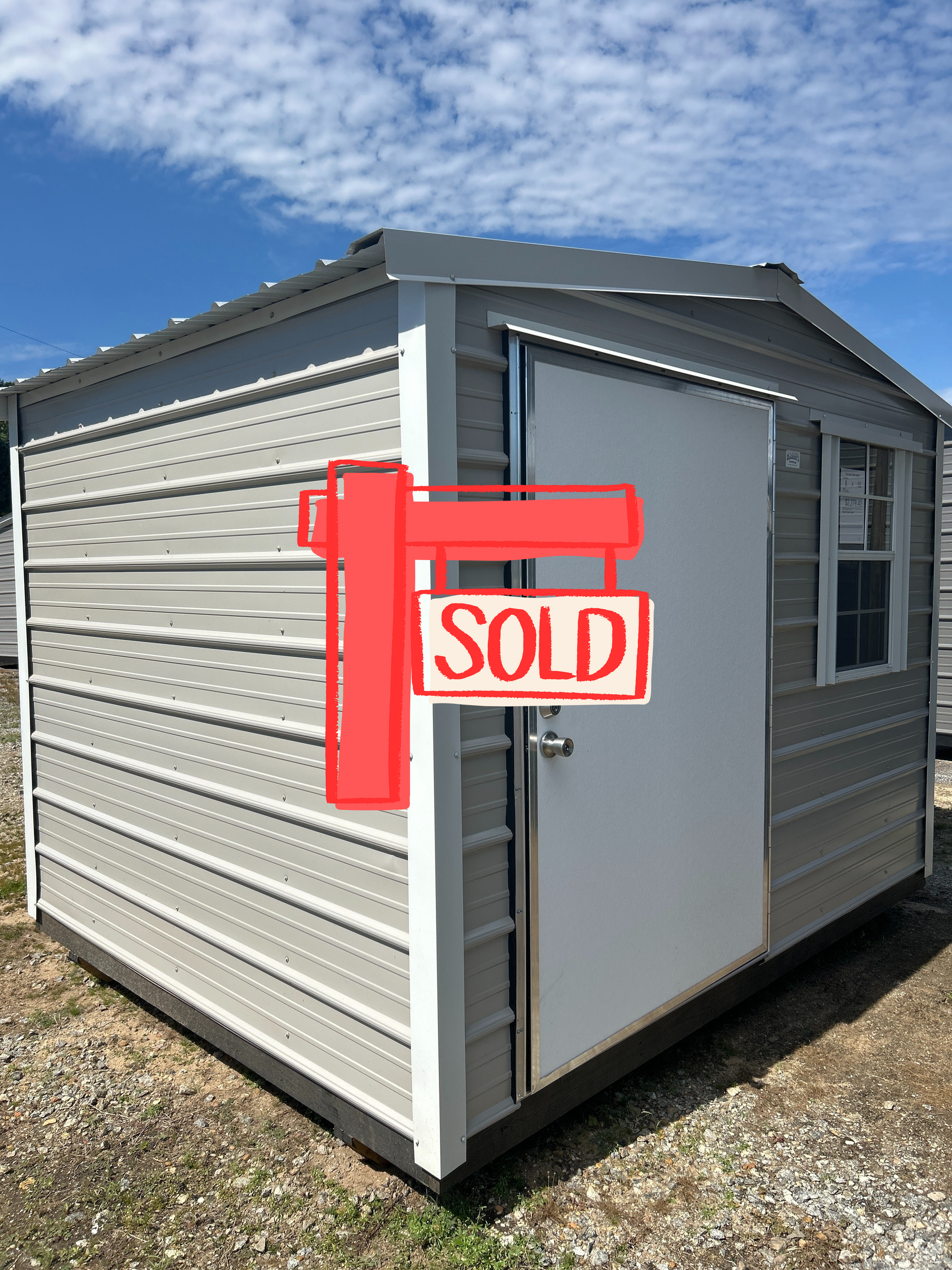 Gray storage shed with white door and trim, small window, under a cloudy sky.