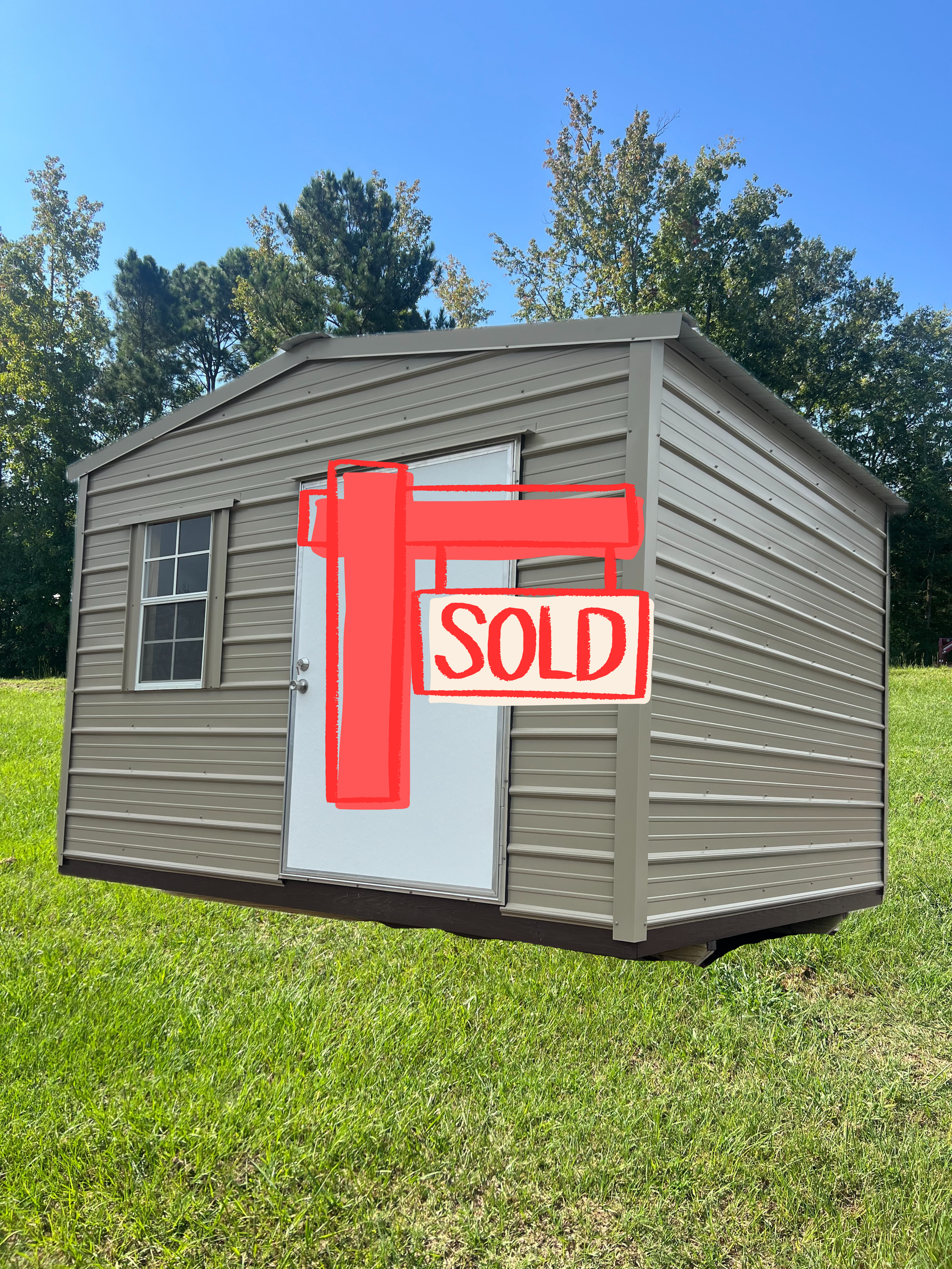 A beige, metal-sided storage shed with a white door and a single window sitting on a grassy lawn under a clear blue sky.
