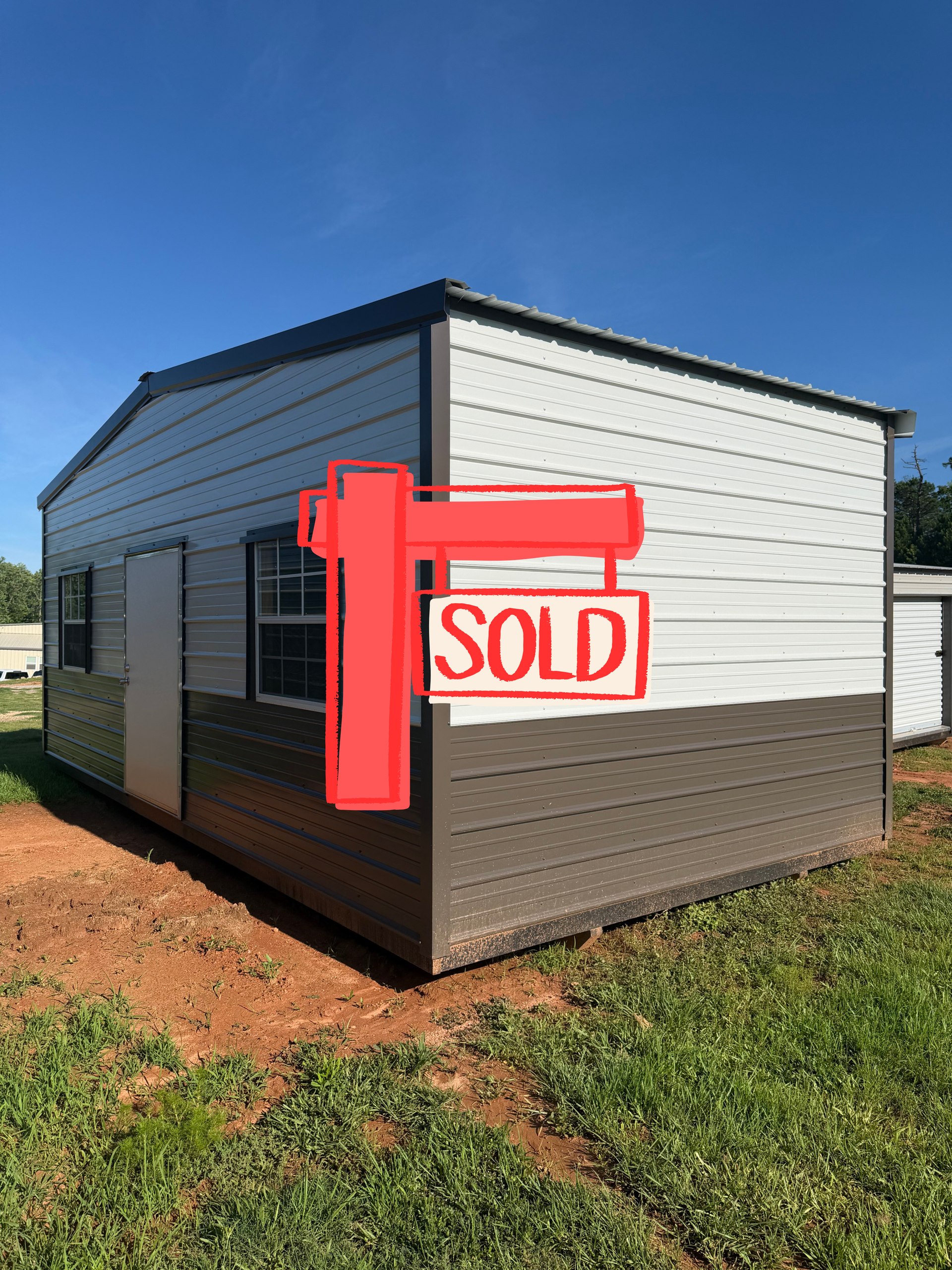 White and black tiny house with a red “SOLD” sign on the front deck under a blue sky