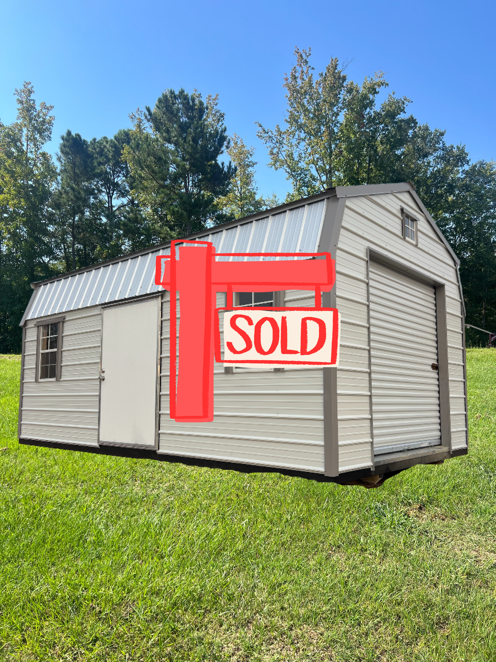 Small white shed with a red SOLD sign on a grassy lawn under a blue sky