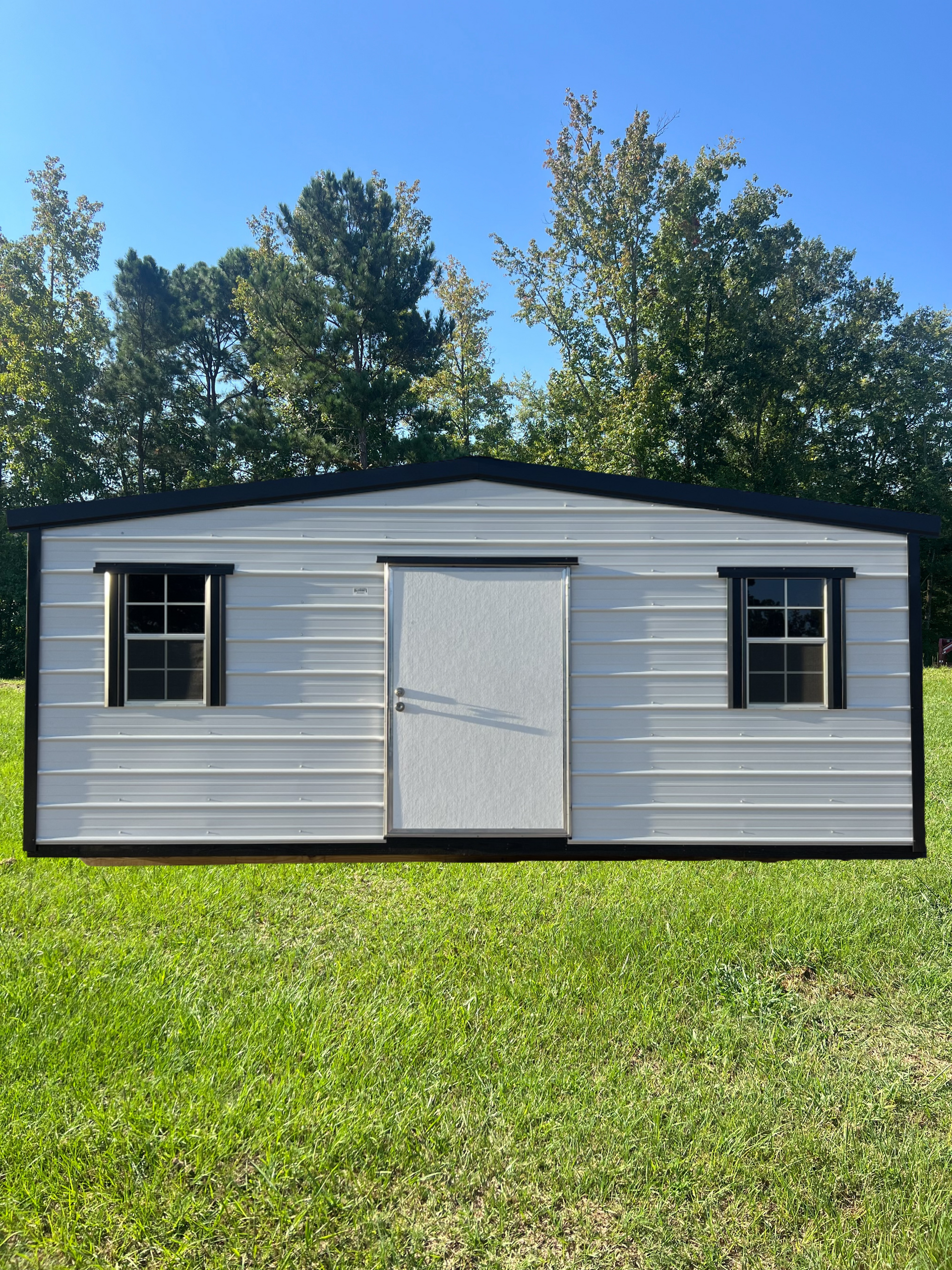 White metal shed with black trim, door, and two windows, set in grassy area.