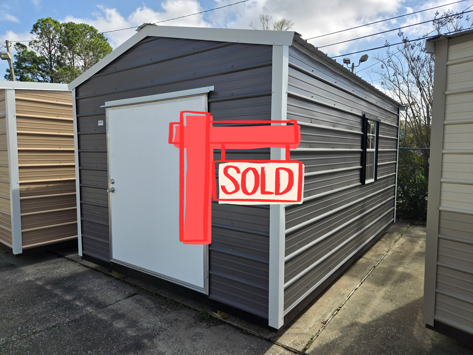 Gray storage shed with white door, window, and trim, on a concrete surface.