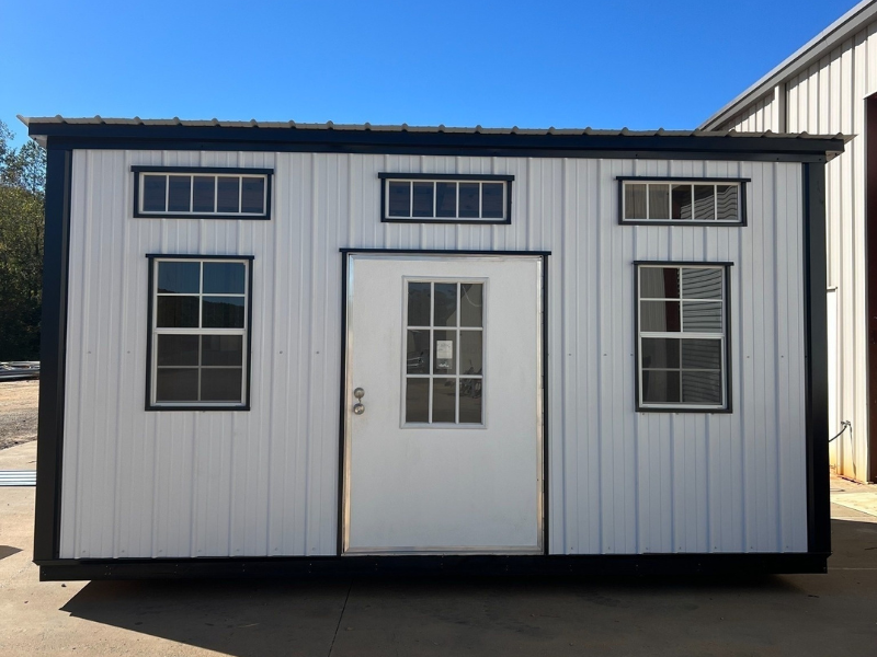 White and black shed-style building with door and windows against a blue sky.