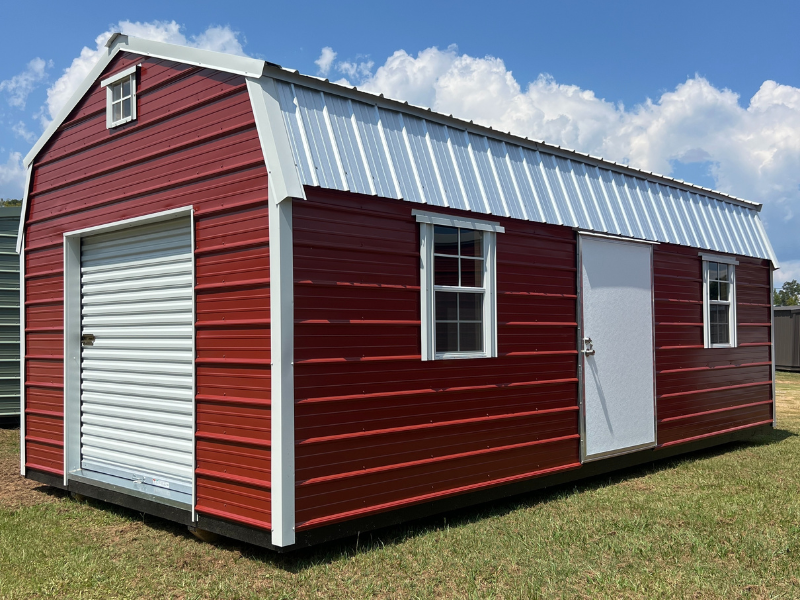 Red barn-style shed with white trim, a roll-up garage door, windows, and a metal roof.