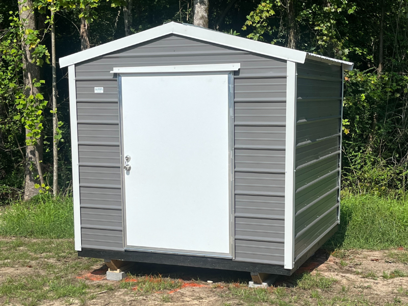 Gray storage shed with white door, set on a grassy area, surrounded by trees.