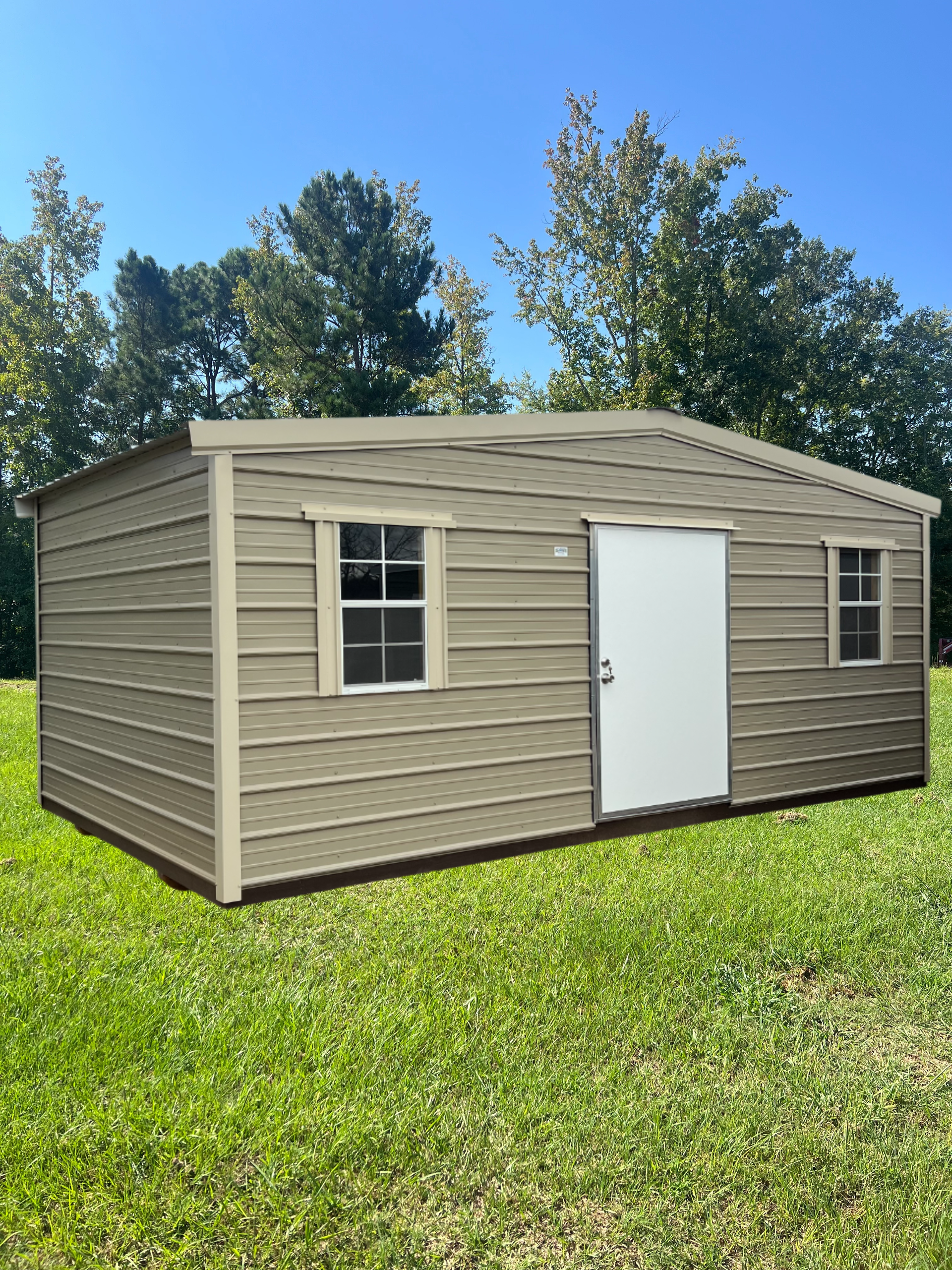 Tan metal shed with white door and windows on green grass.