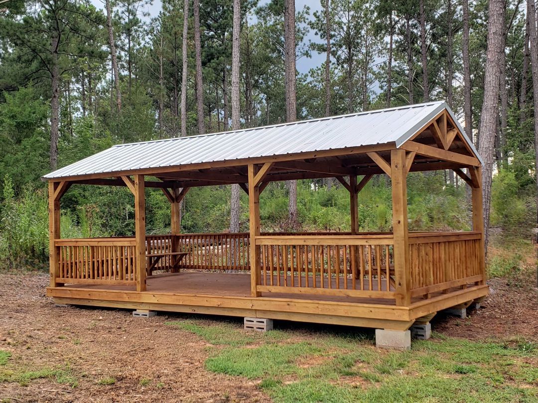 A wooden gazebo with a metal roof is sitting in the middle of a field.