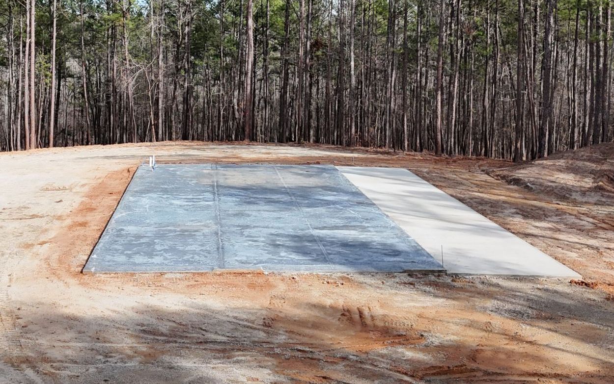 Concrete foundation in a dirt clearing, surrounded by trees.