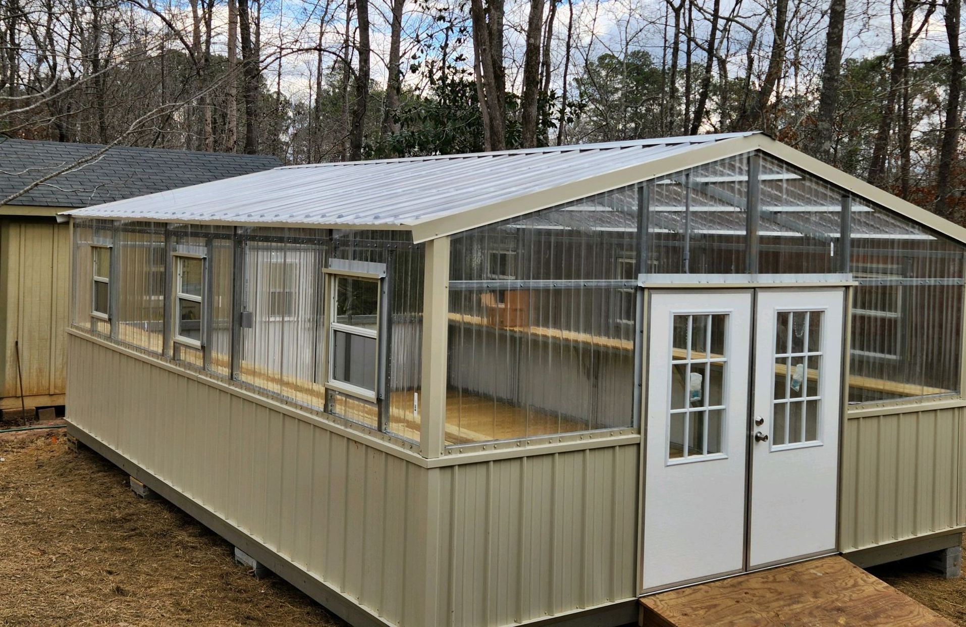 A greenhouse is sitting in the middle of a dirt field next to a house.
