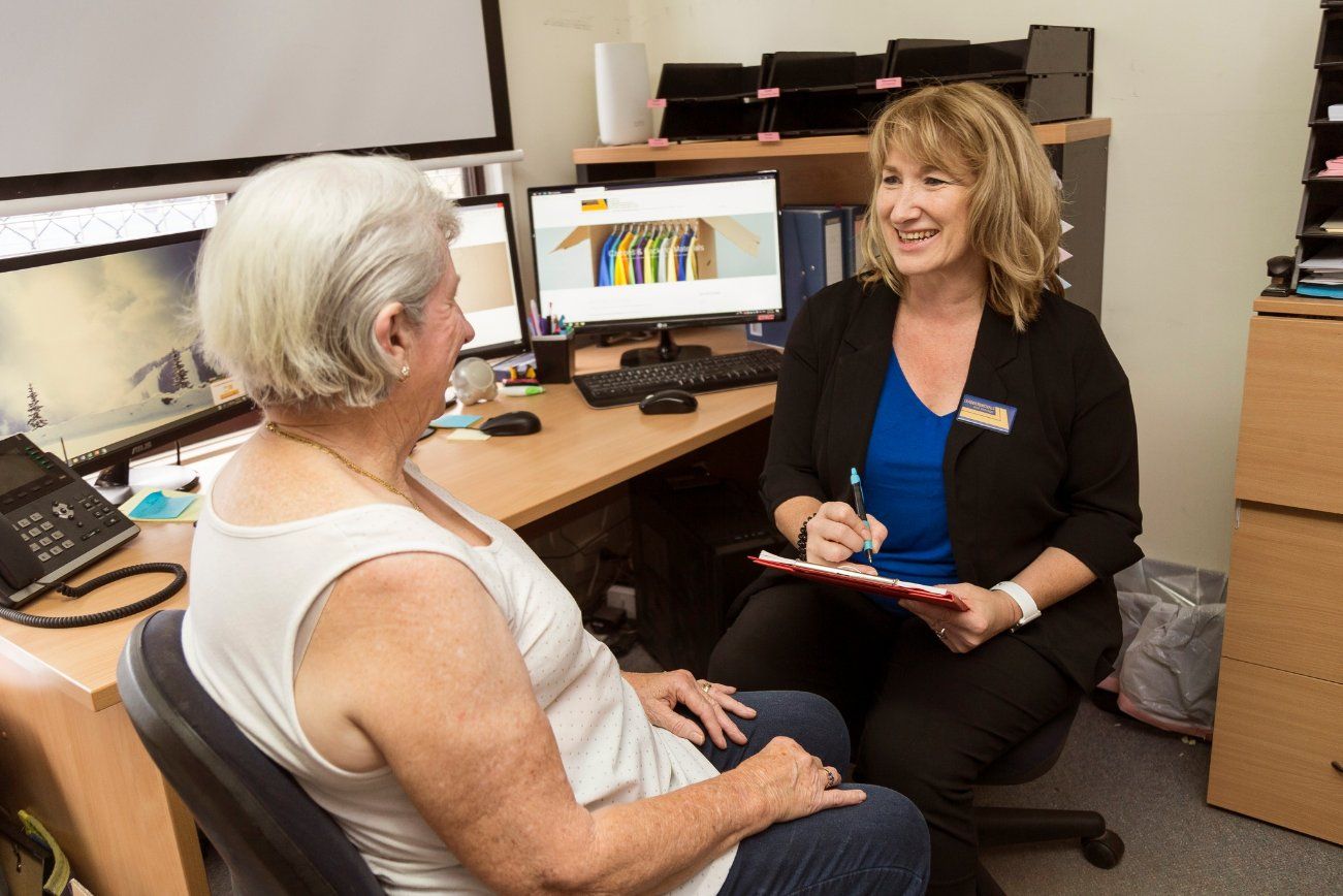 A Woman Is Sitting at A Desk Talking to An Older Woman — Leader Removals & Storage in Mitchell, ACT