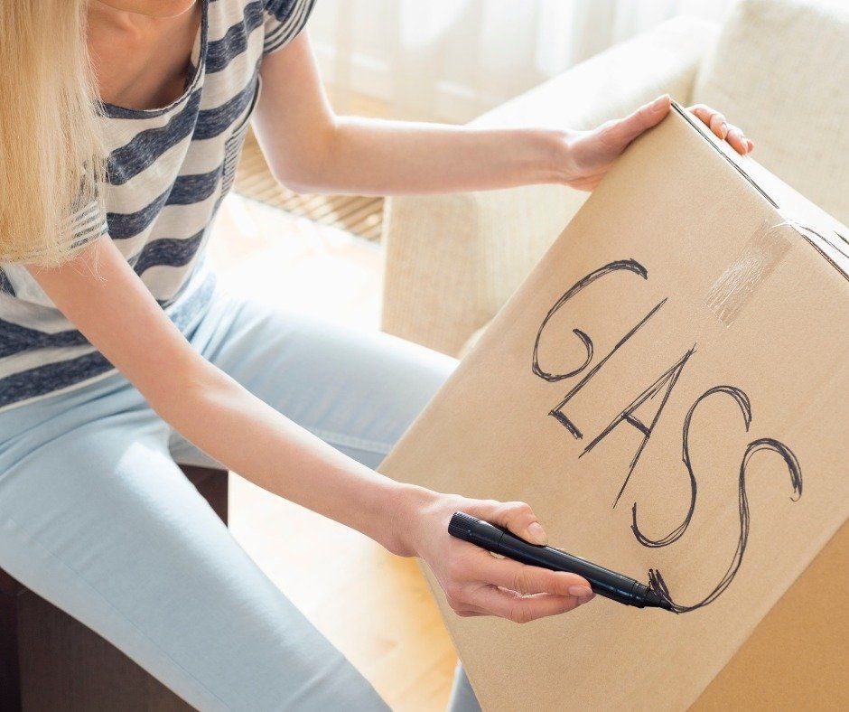 A woman is writing the word glass on a cardboard box — Leader Removals & Storage in Mitchell, ACT