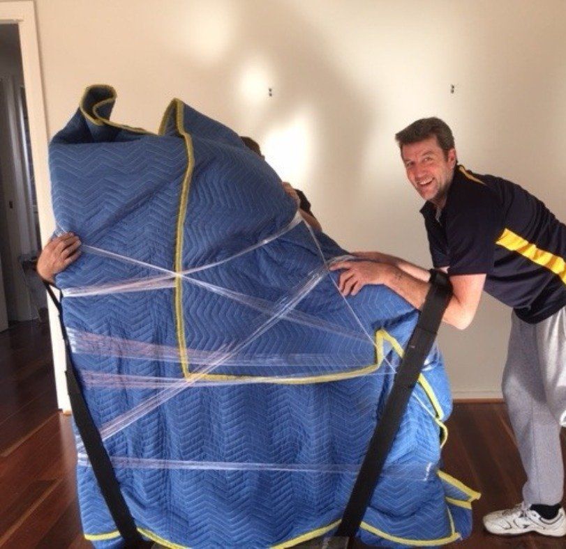 A Man Is Holding a Blue Blanket that Is Wrapped in Plastic — Leader Removals & Storage in Mitchell, ACT