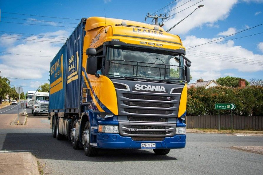 A Blue and Yellow Scania Truck is Driving Down a Street — Leader Removals & Storage in Bowral, NSW