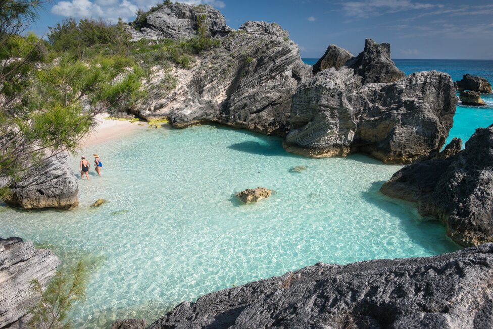 A couple of people are standing in a small body of water surrounded by rocks.