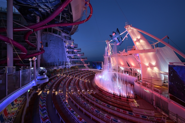 A large amphitheater on a cruise ship with a water slide in the background.