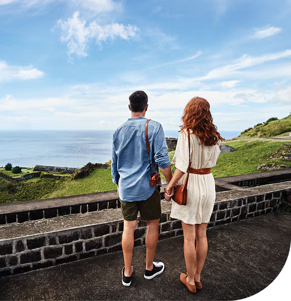 man and lady couple standing looking at the ocean beside a stone wall