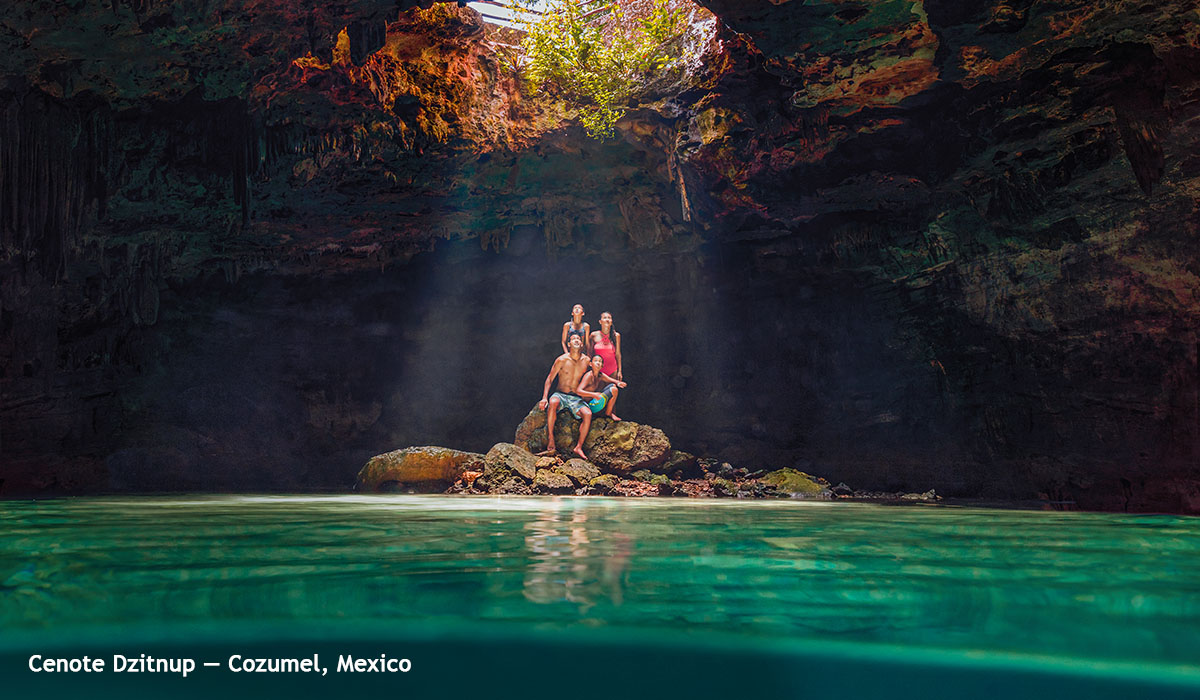 three people in mddle of green water in a cave standing on a rock