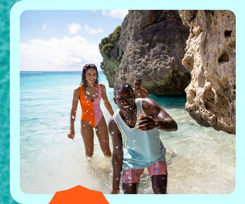 man and lady plying in the beach water with sand rocks and ocean behind them