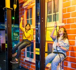 Two women are sitting on a swing in front of a brick wall.