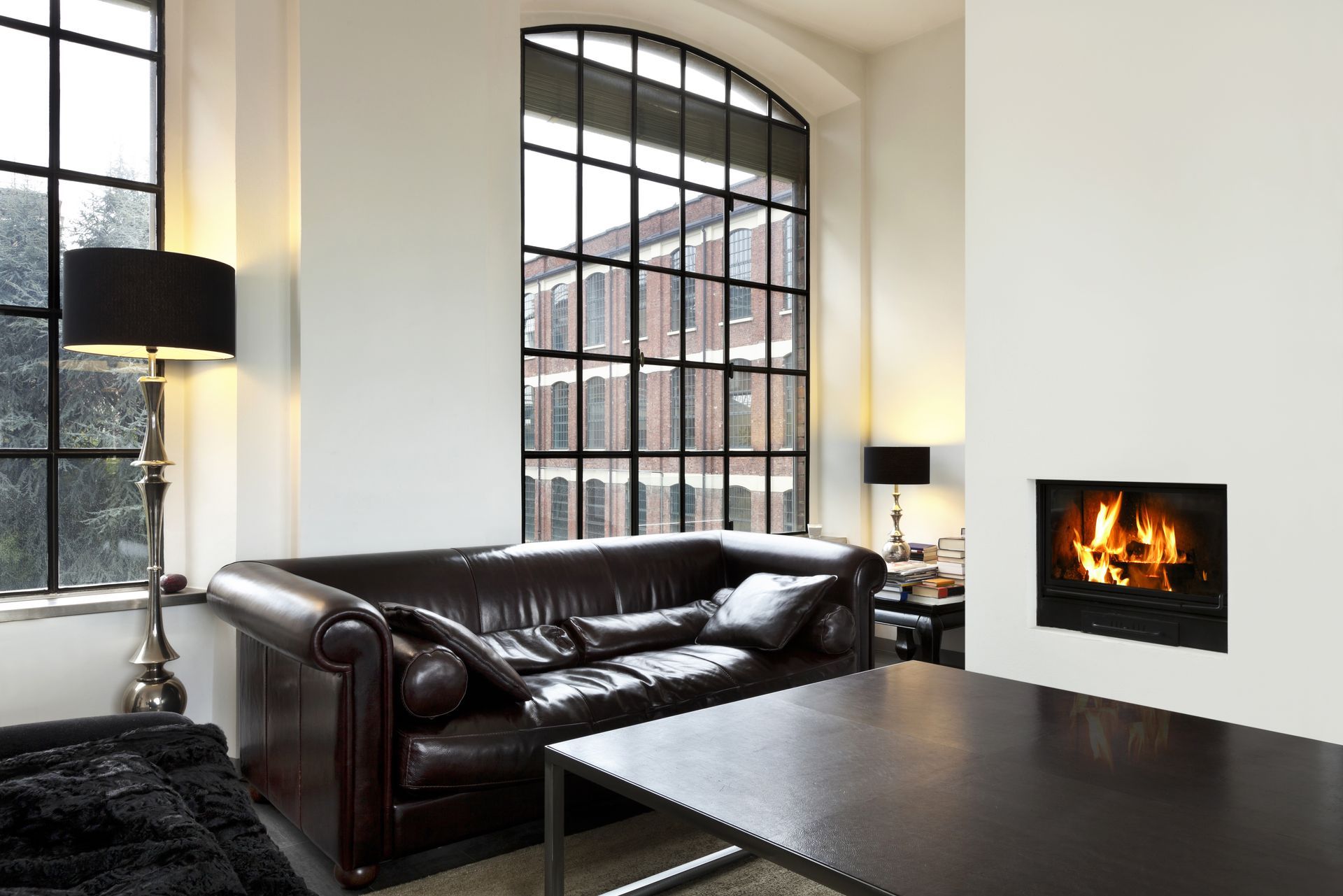 Living room with leather sofa, fireplace, large windows, and black lamps.
