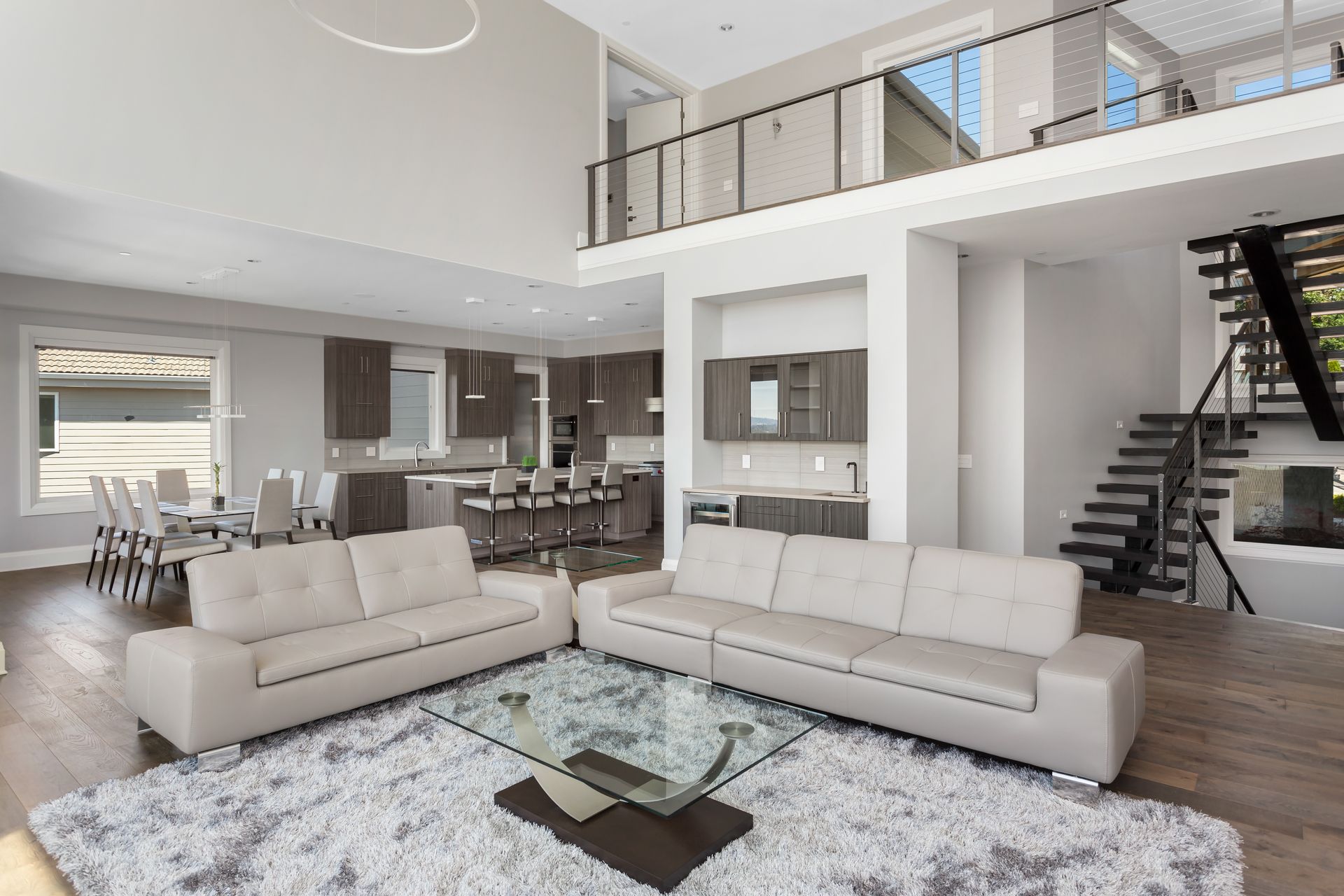 Spacious modern living room with neutral colors, two sofas, a rug, and a kitchen visible in the background.