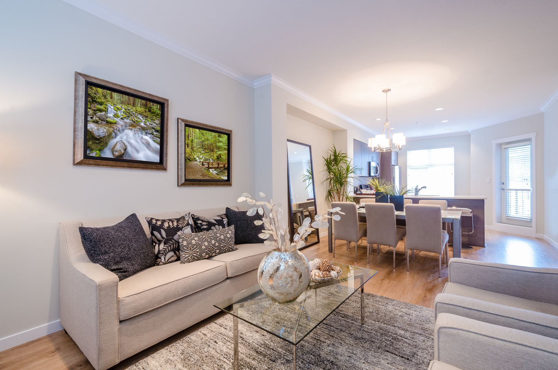 Living room with a beige sofa, area rug, glass coffee table, and dining area in the background.