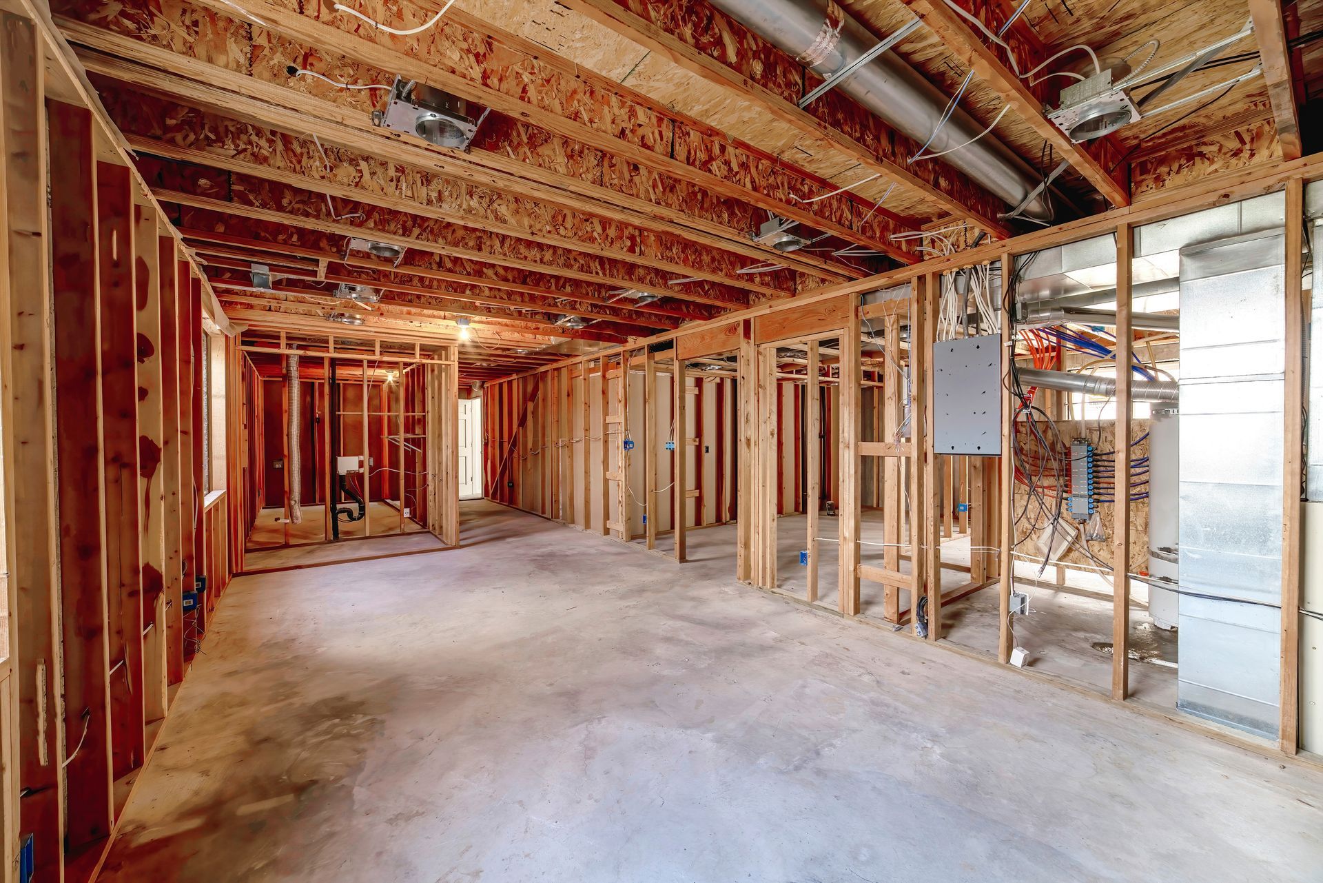 Interior of a room under construction, with wooden studs and exposed ceiling beams. Concrete floor.