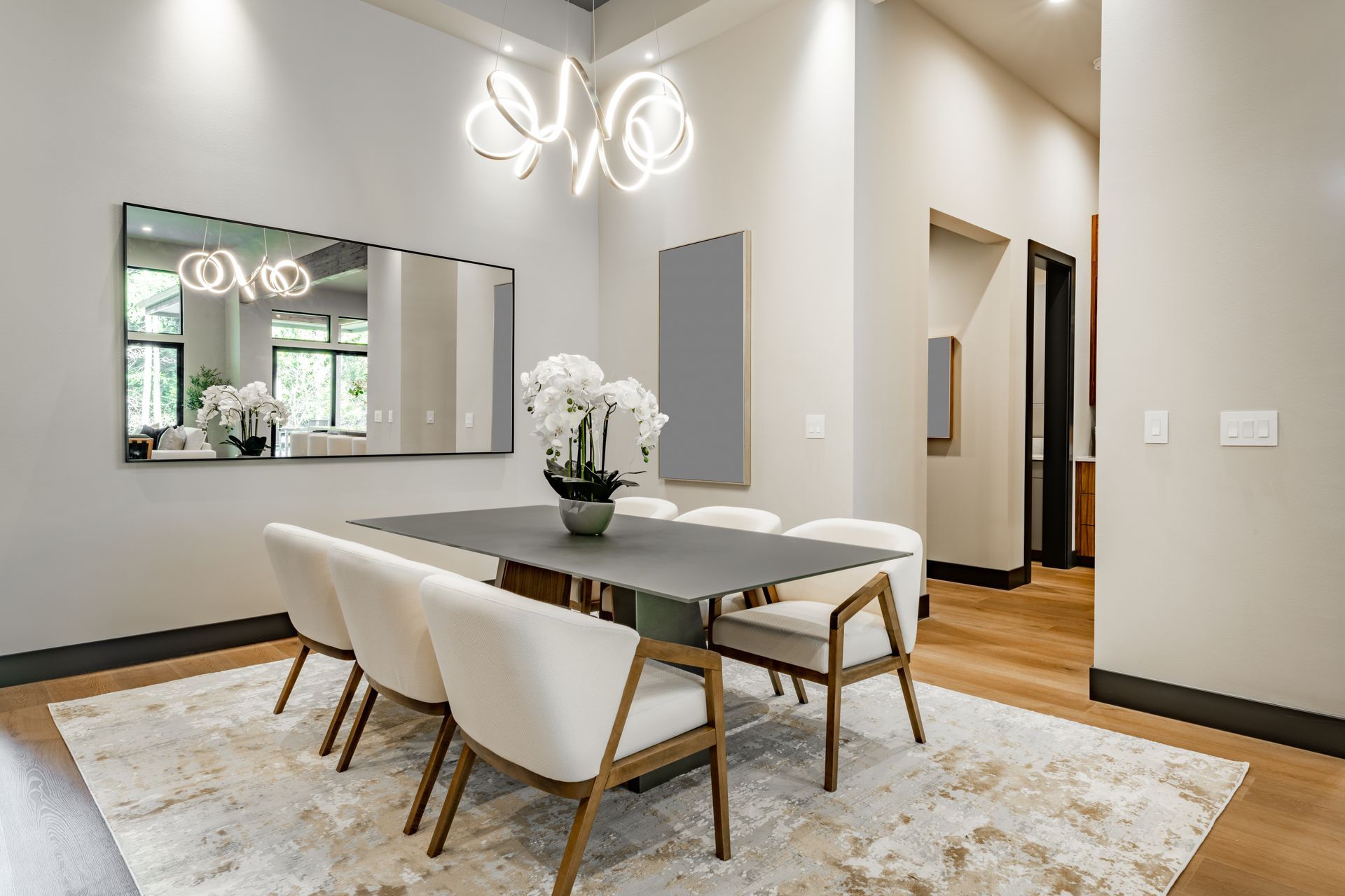 Dining room with table set for six, neutral tones, modern chandelier, large mirror, area rug.