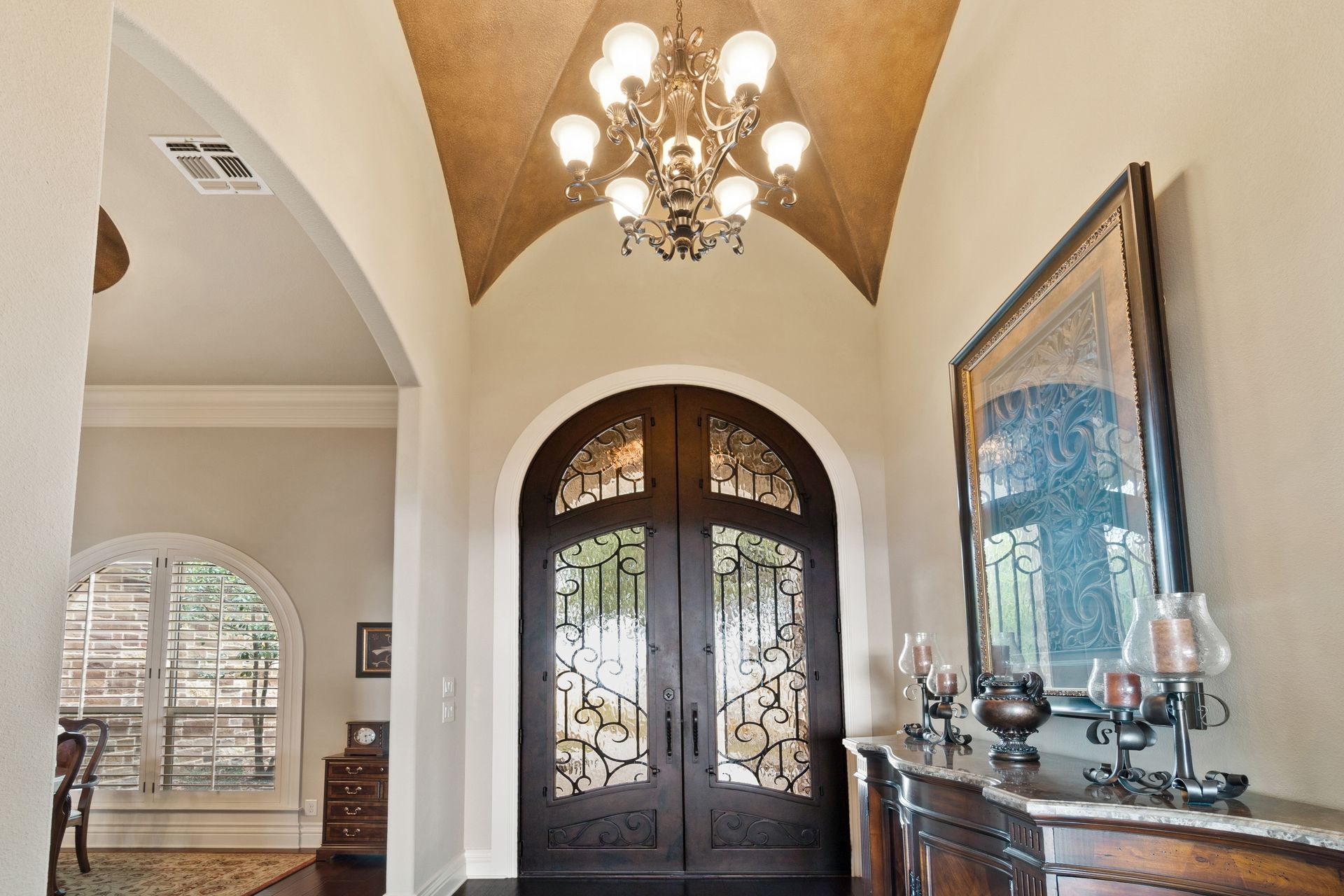 Elegant entryway with arched doorway, double doors with ironwork, chandelier, and a decorative console table.